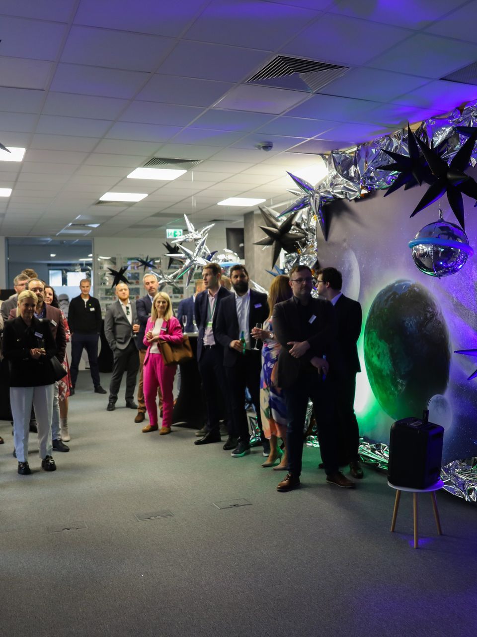 People gathered in a room decorated with disco ball accents, some wearing suits and formal attire.