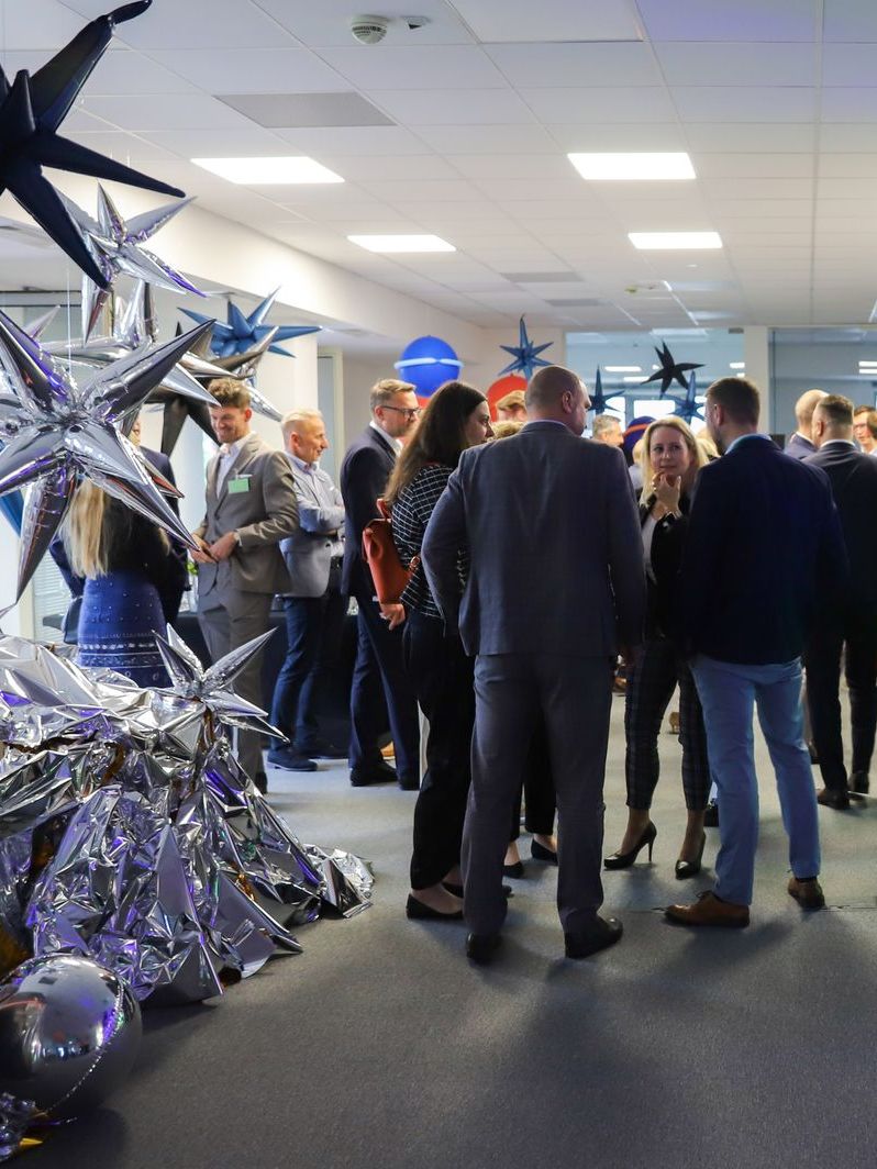 People in a brightly lit hallway decorated with star-shaped balloons, conversing.