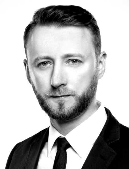 Mężczyzna w garniturze, patrzący w kamerę z poważnym wyrazem twarzy, zbliżenie, czarno-białe zdjęcie.
