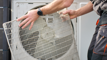 Technician connecting hoses to an outdoor air-conditioning unit with tools and gauges