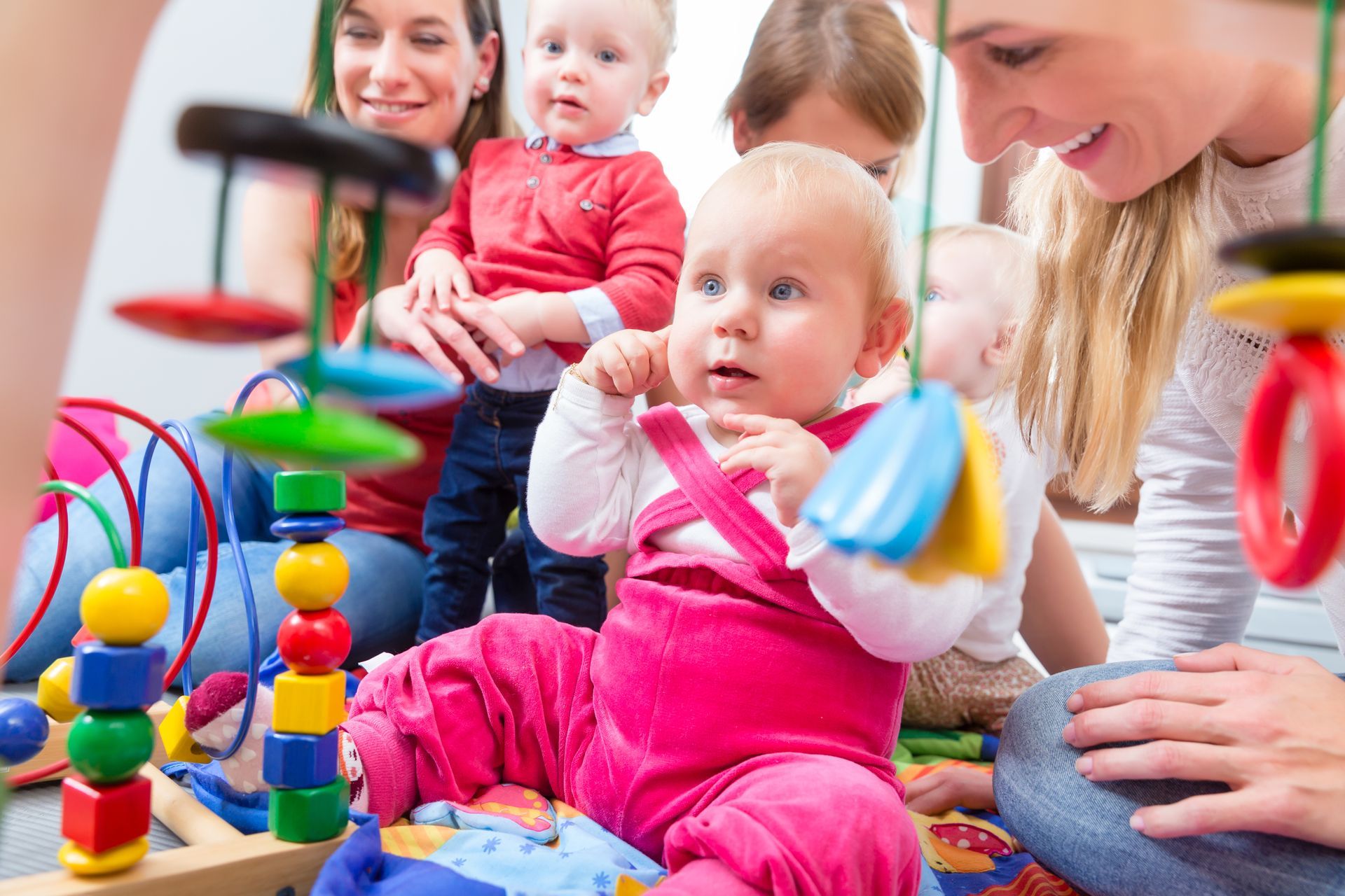 Portrait of a cute baby girl while sitting down on the floor with two other babies and their carers. Portrait of a cute baby girl while sitting down on the floor with two other babies and their carers.