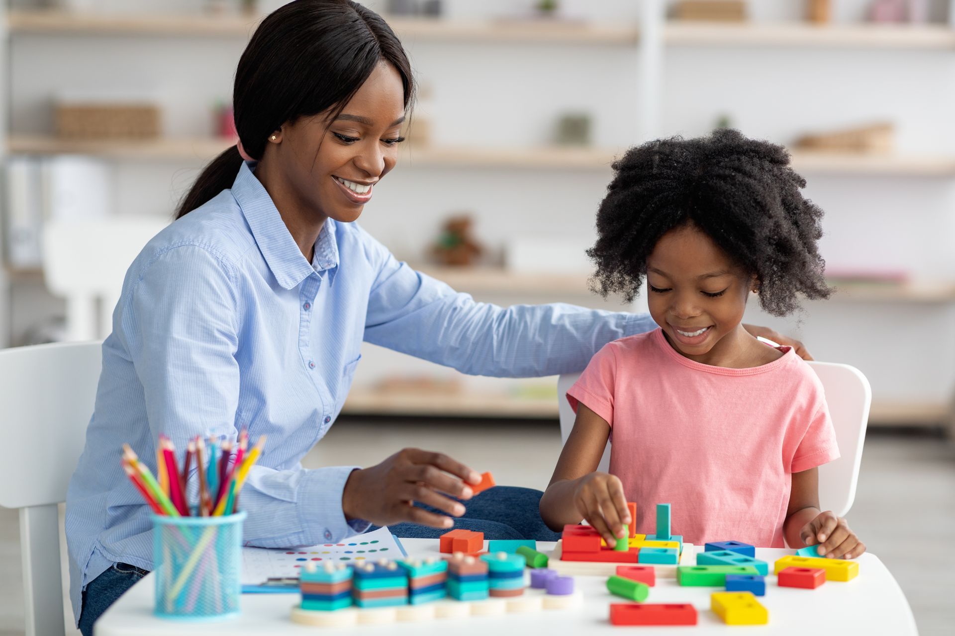 Pretty black kid and child development specialist playing with bricks.