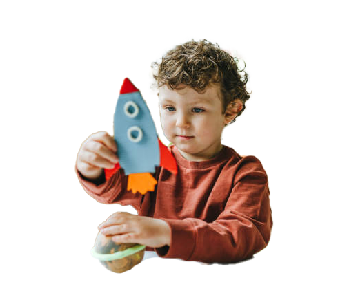 Young child holding a blue and red rocket and a planet toy; white background. Young child holds a toy rocket ship and planet. He is looking at them intently, wearing a red shirt.