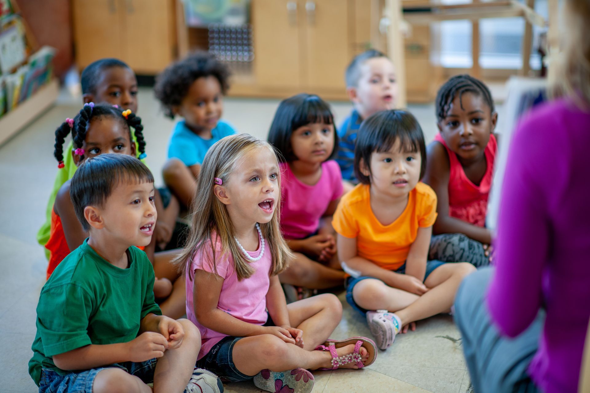 An academy teacher sits with her students in front of her as she reads the group a story.