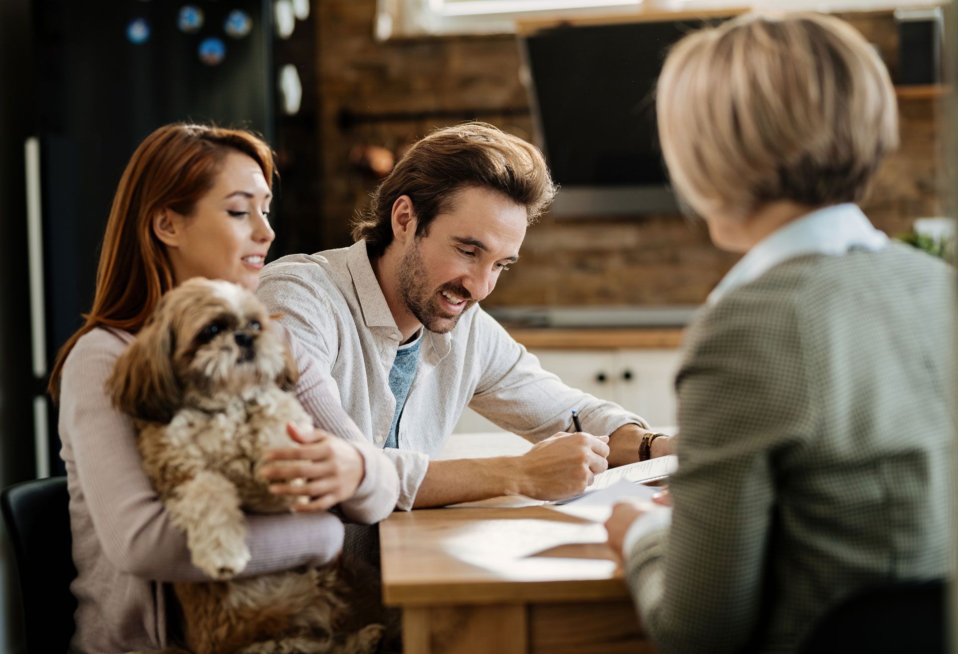 Family meeting with a fluffy dog at a table, as a man writes while two others listen in a cozy room