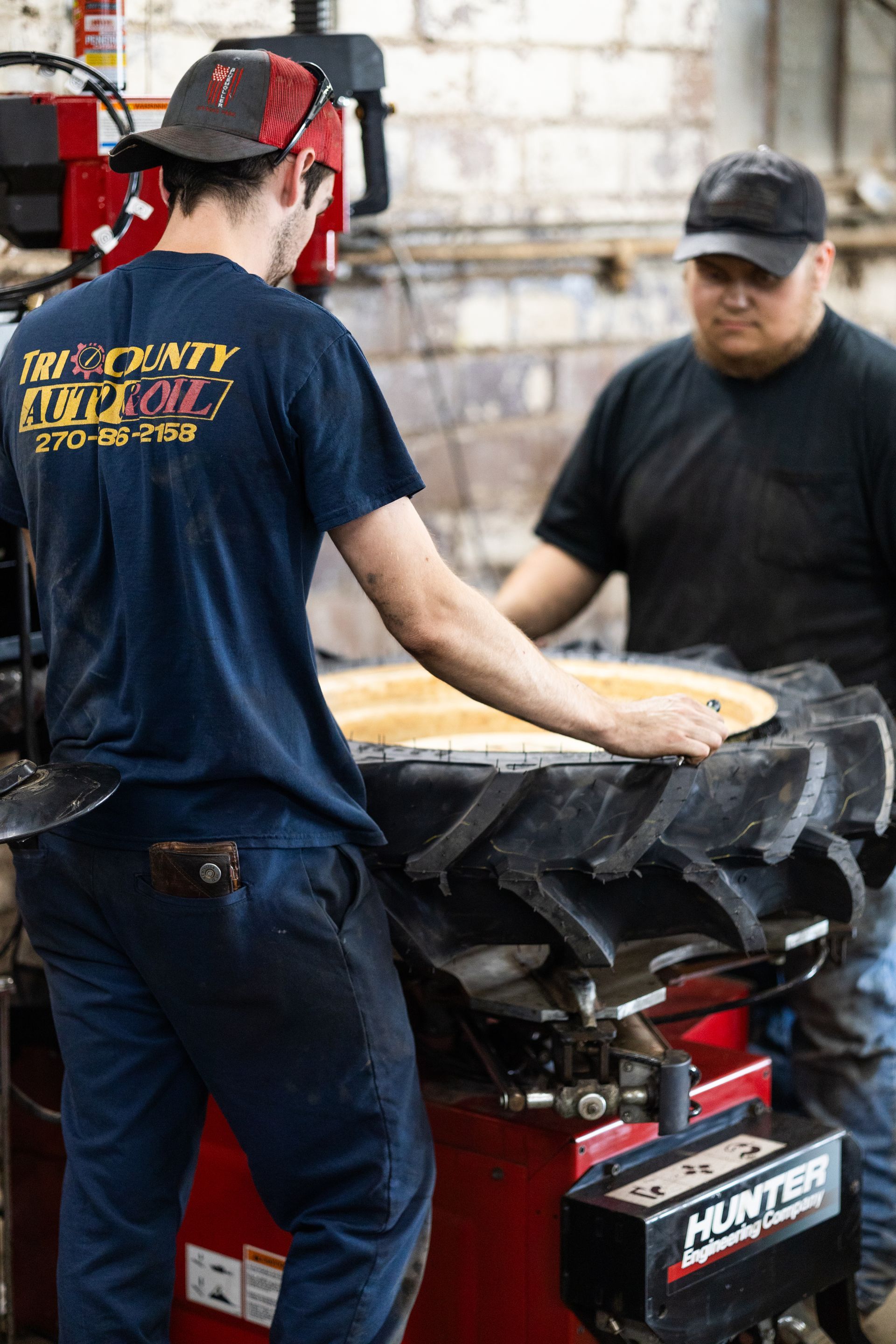 Two service mechanics are working on a tire in a garage.