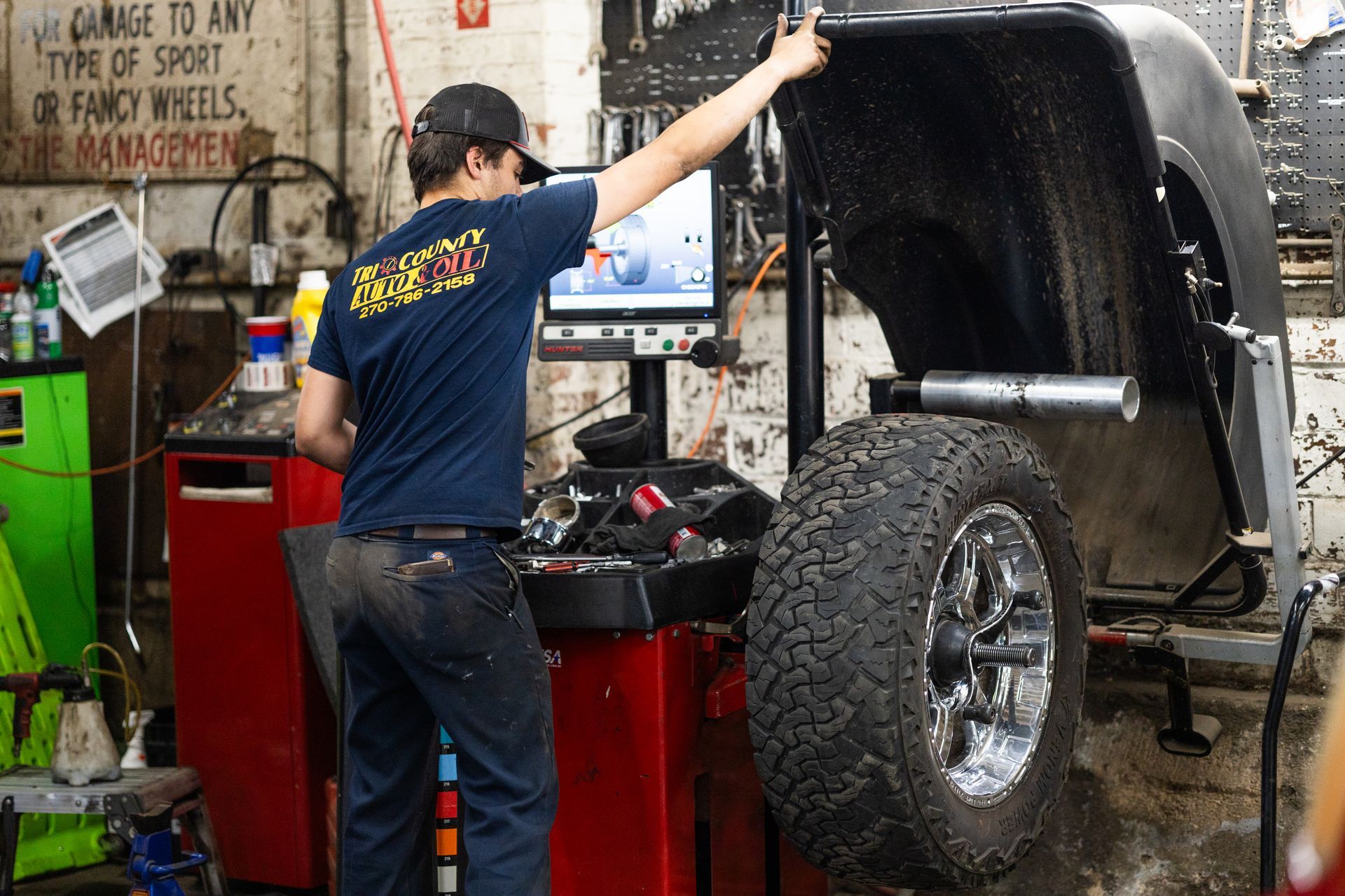 A service mechanic is working on a tire in a garage with a sign that says garage is any type of sport or fancy wheels