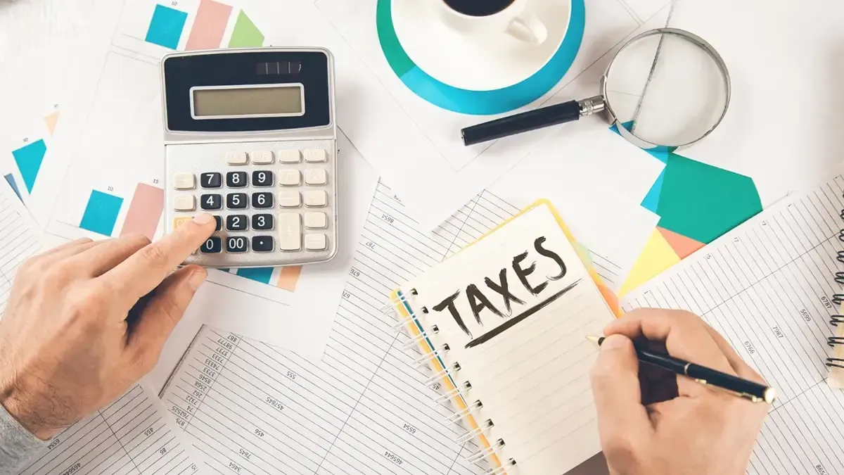 Man writing taxes text on notepad with calculator on document
