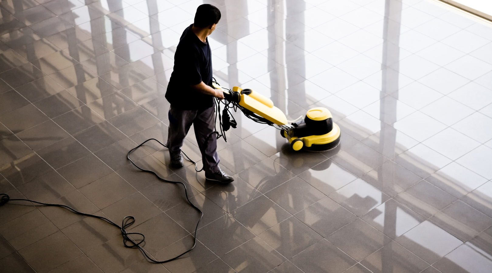 A man is cleaning a tiled floor with a machine.