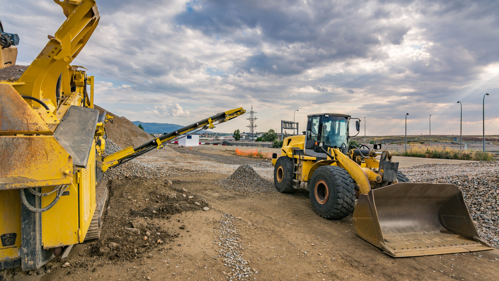 Yellow construction machinery on a dirt worksite under cloudy skies