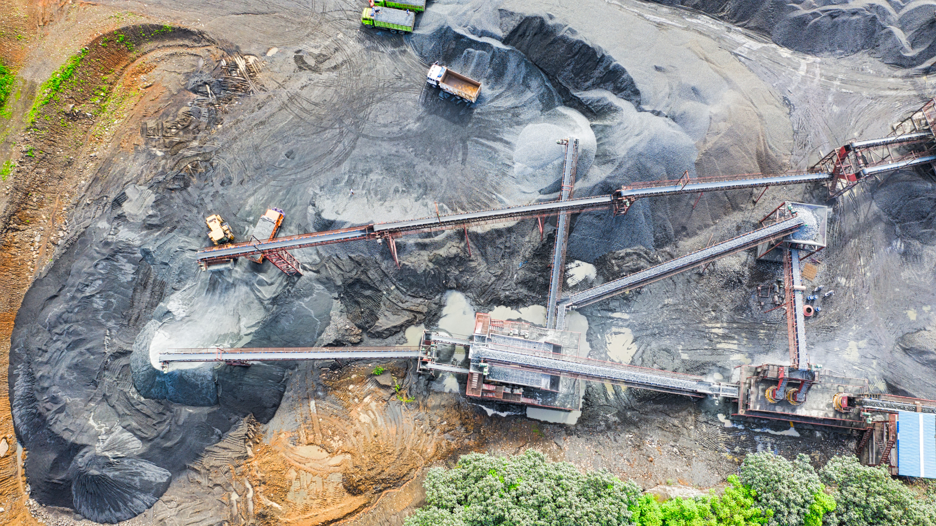 Aerial view of a mining conveyor system moving dark material through a wet, muddy quarry