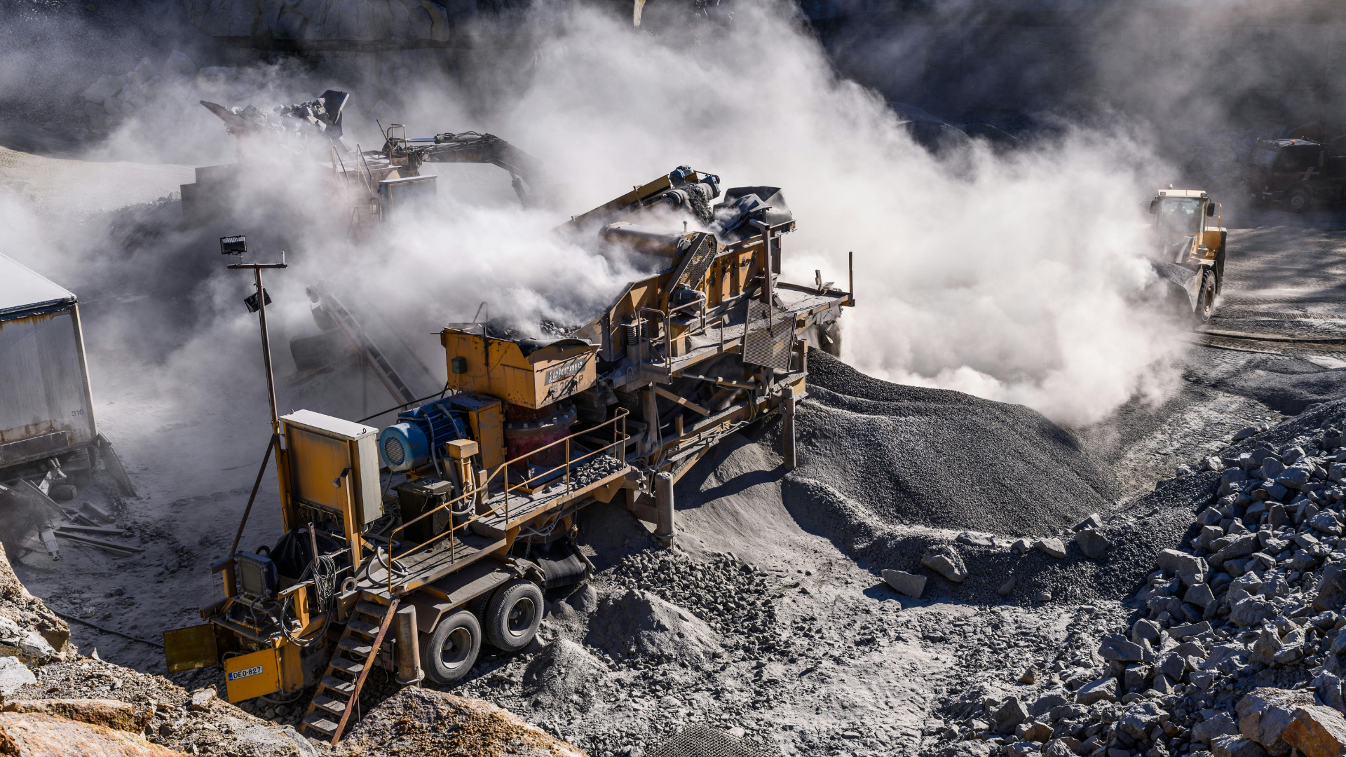 Large yellow mining machine amid dark rubble and thick white dust at an open-pit mine
