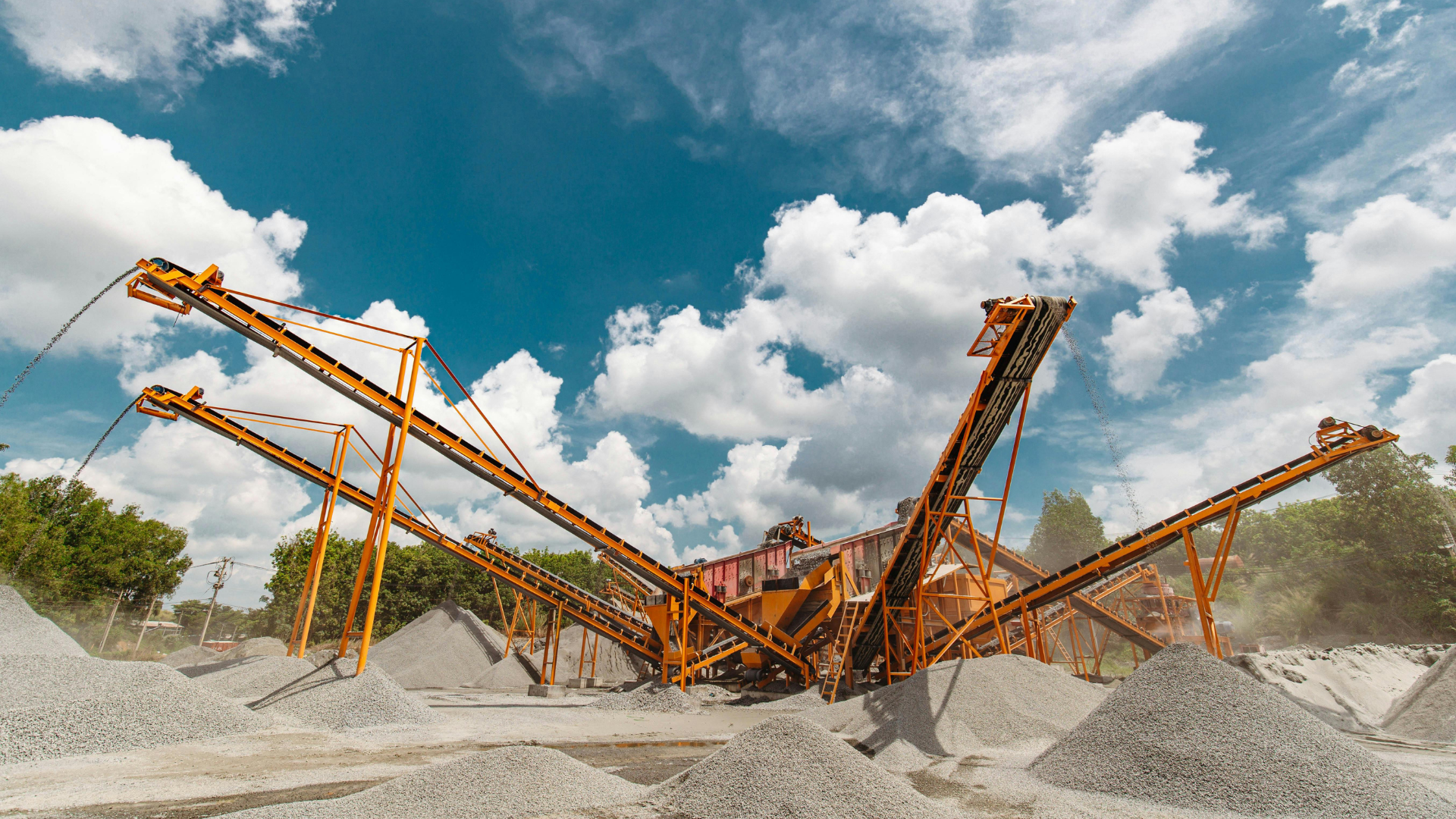 Orange industrial conveyor machinery at a gravel quarry under a cloudy blue sky