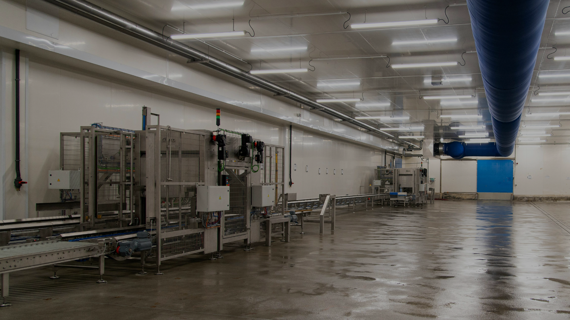 Industrial warehouse interior with stainless steel machinery, wet floor, and bright overhead lighting