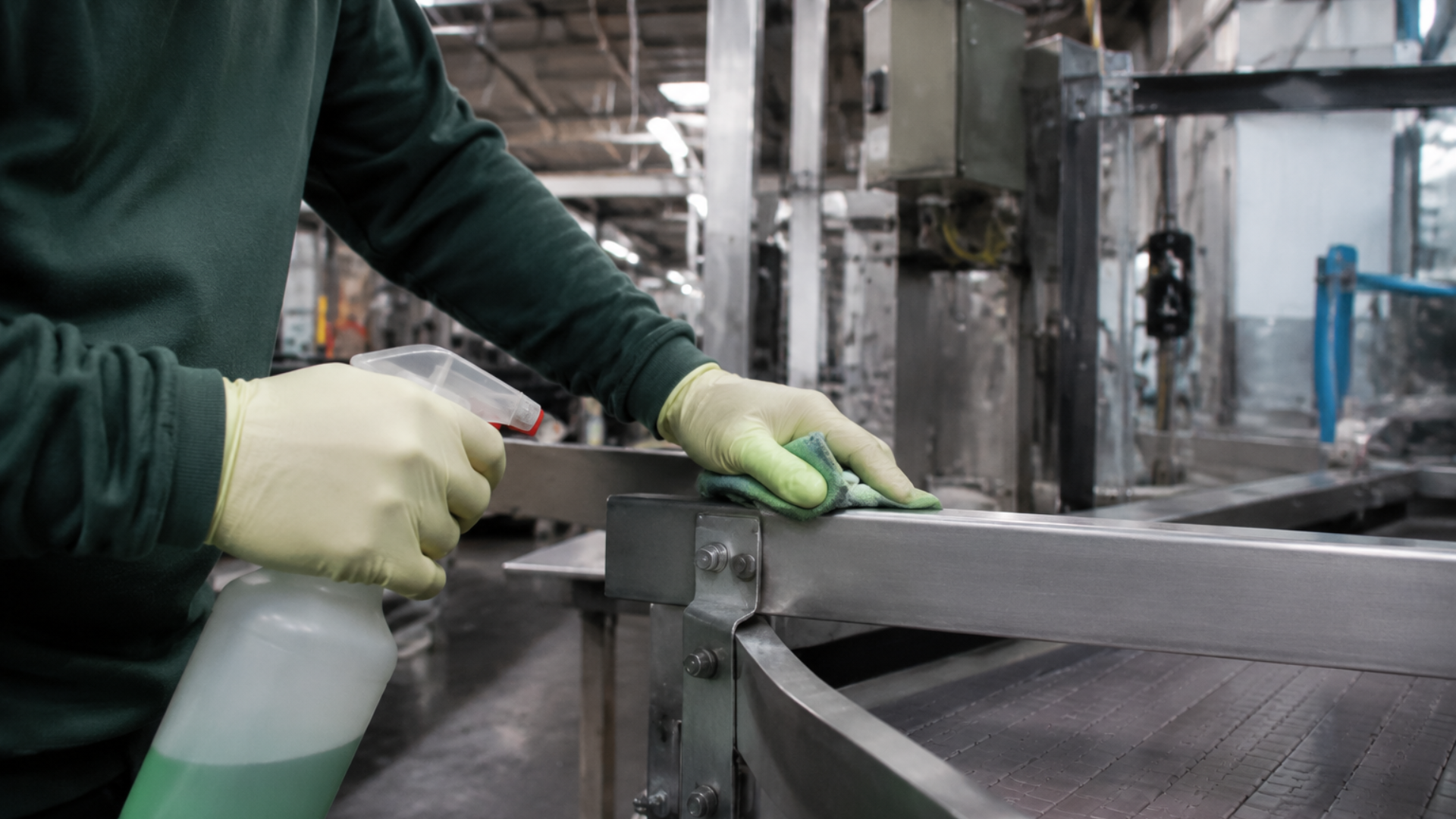 Worker in gloves spraying a metal frame in an industrial workshop.