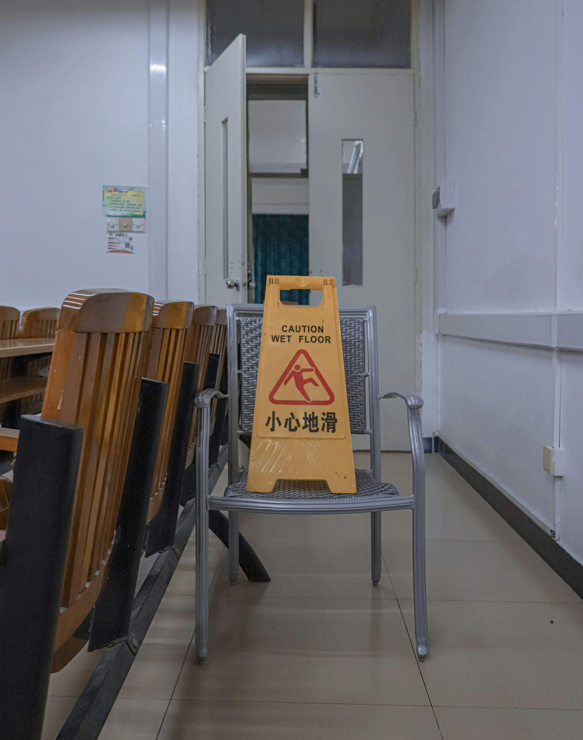 A yellow wet floor sign on a chair in a hallway with wooden chairs.