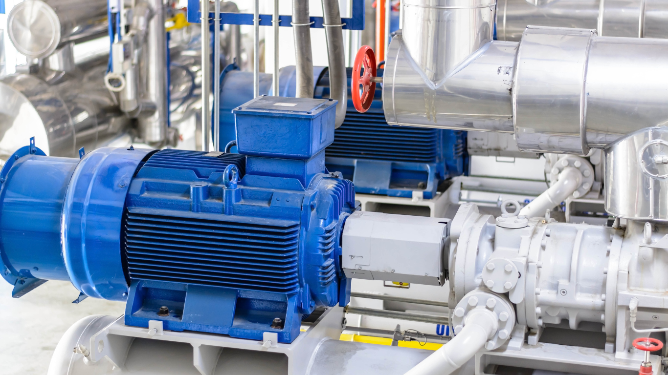 Blue industrial pumps connected to metallic pipes in a factory setting.