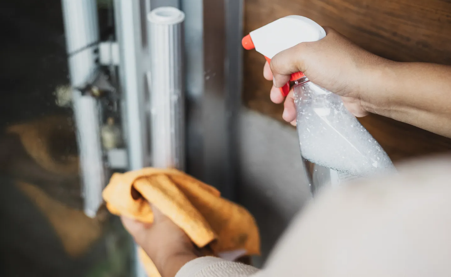Person spraying cleaner onto a door handle, holding a yellow cloth.