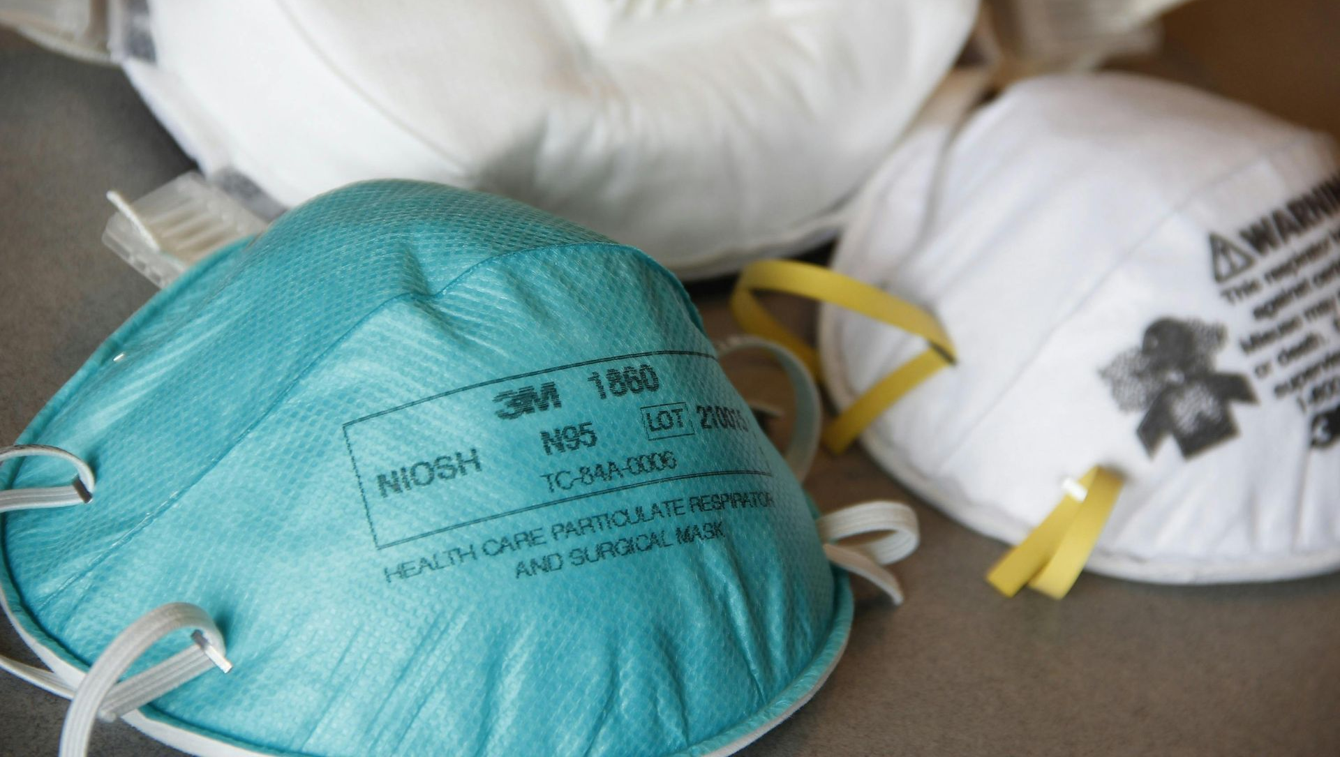 Three N95 respirator masks; one teal, two white.