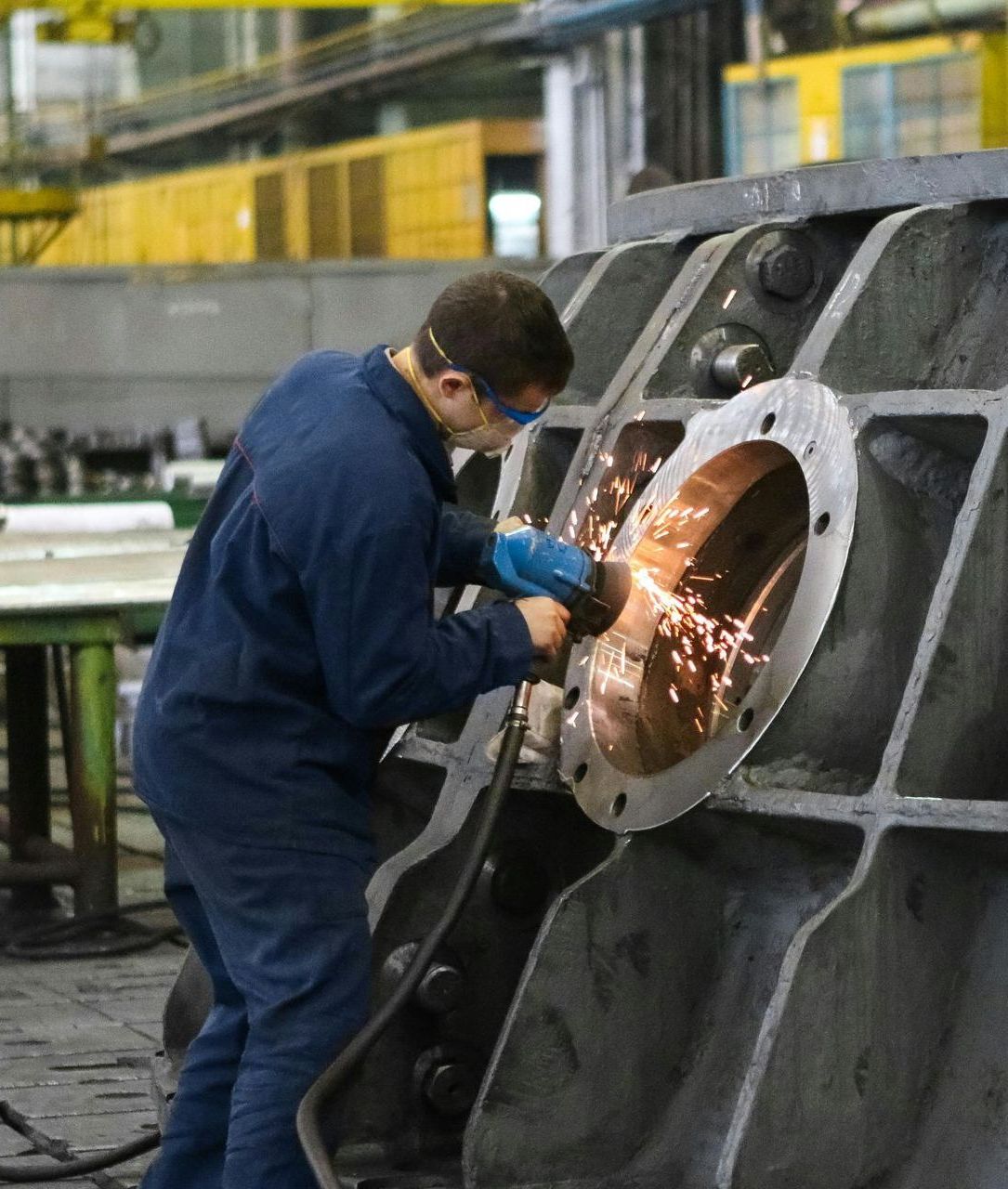 A man in a blue jumpsuit is grinding a piece of metal