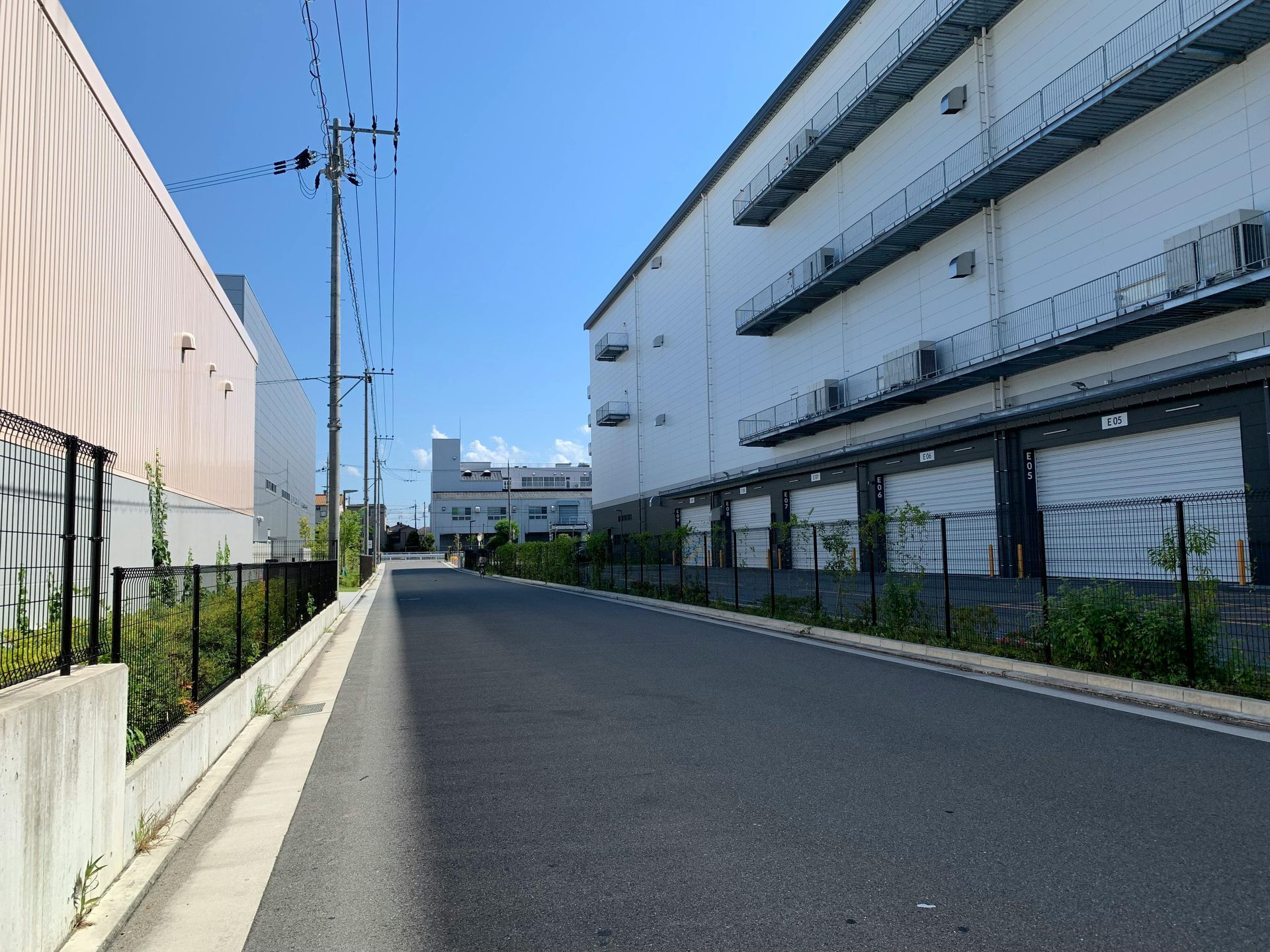 Empty asphalt road between two industrial buildings, blue sky overhead.
