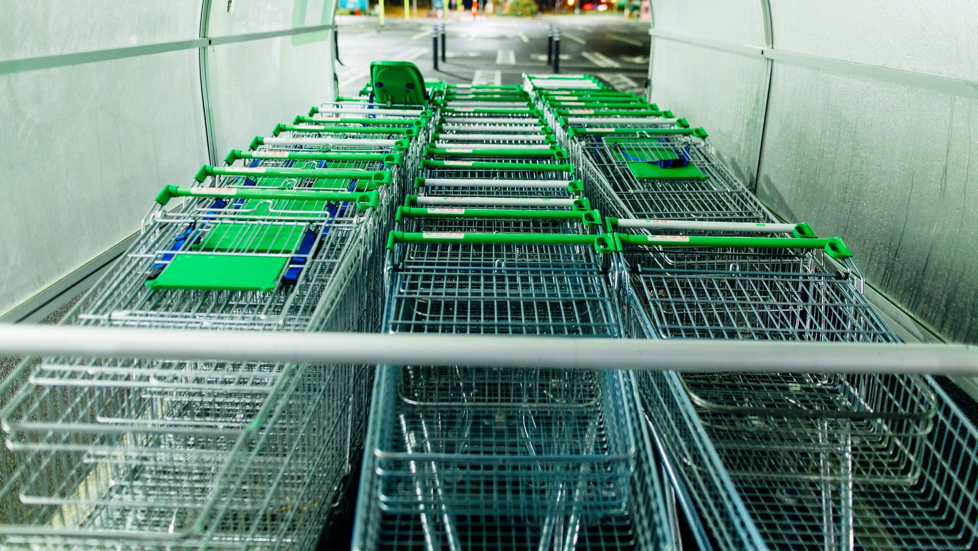Rows of green and silver shopping carts are neatly stacked together in a sheltered area.