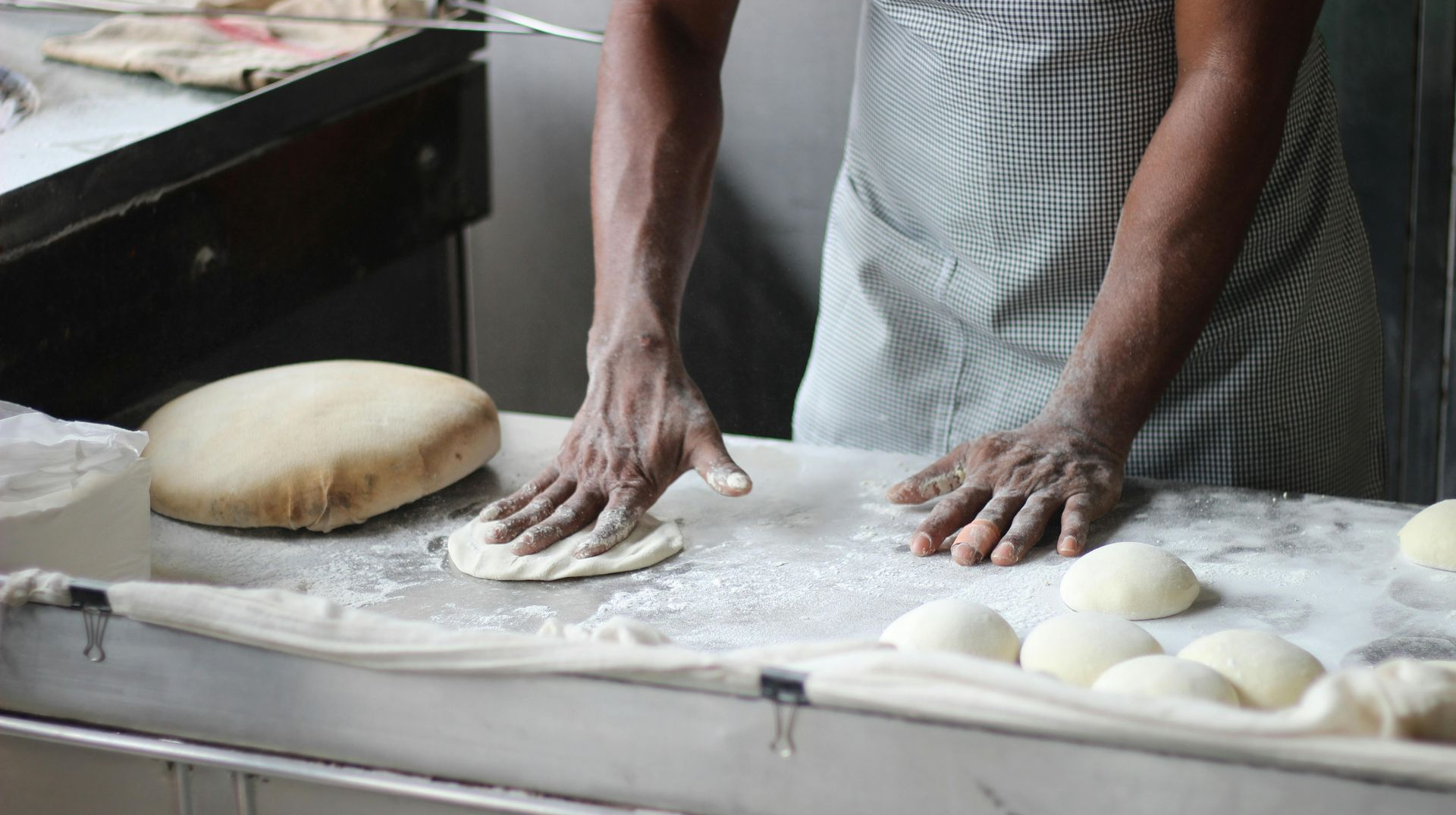 Baker rolling out dough on a floured surface, with bread rolls nearby.
