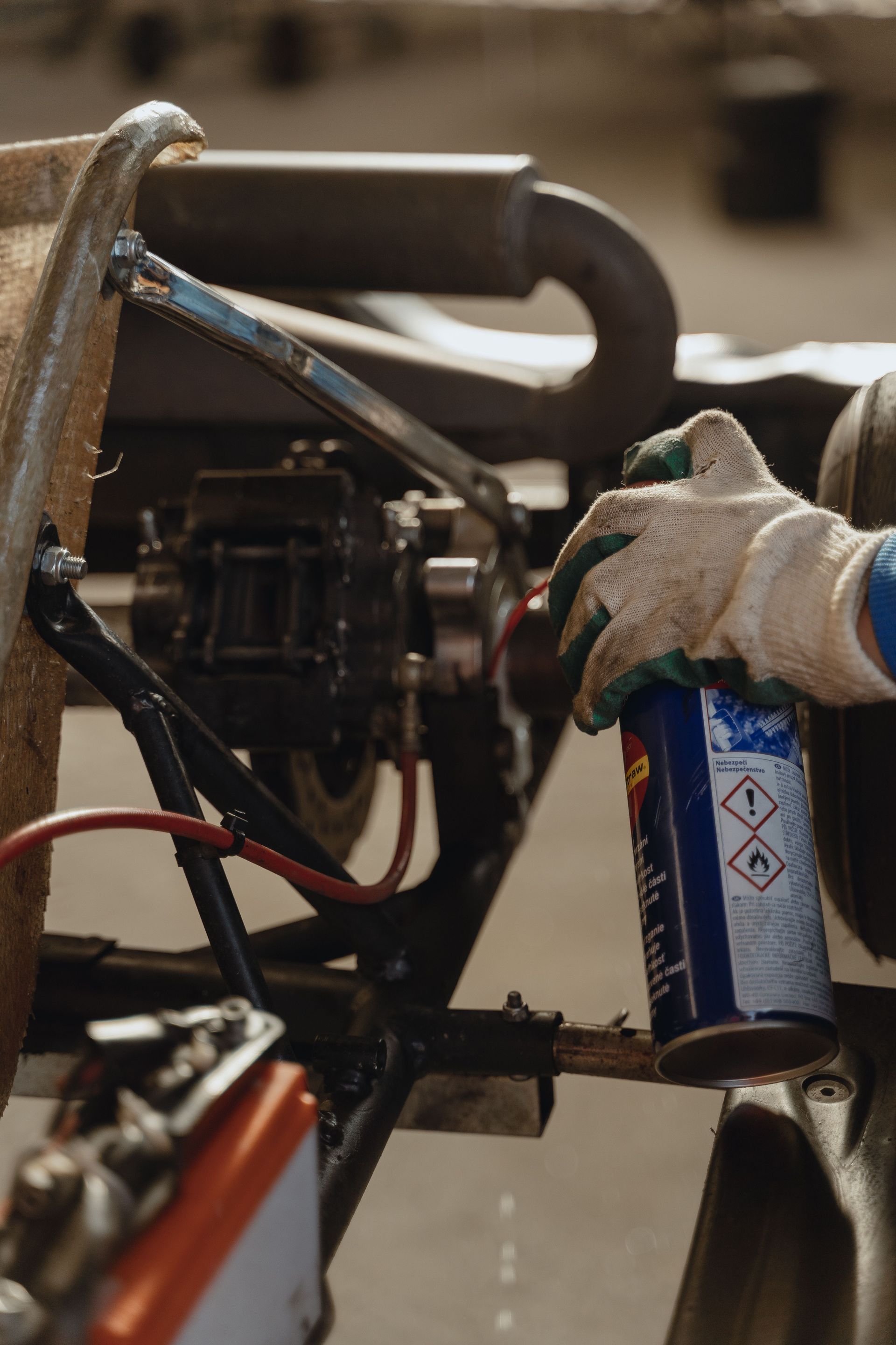 Gloved hand holding a blue canister beside machinery or a vehicle frame