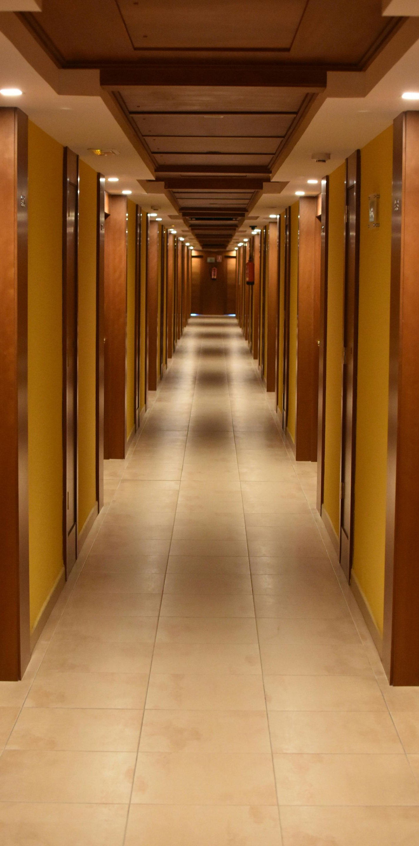 Hotel hallway with doors on both sides, yellow walls, and wooden frames.