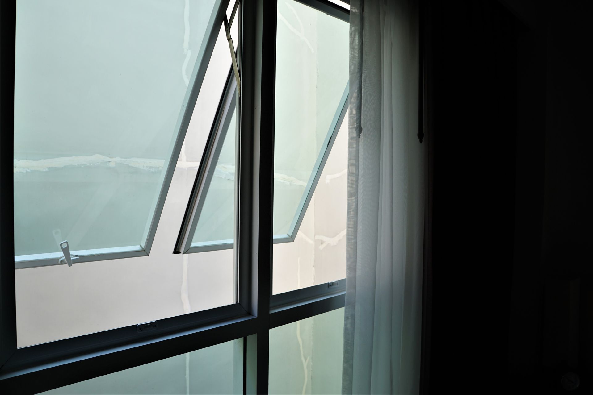 A large window with a white curtain is open in a dark room.