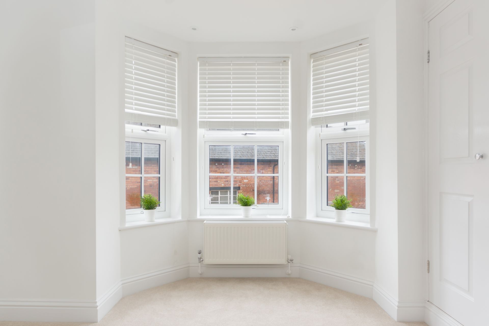 An empty room with a bay window and white blinds.