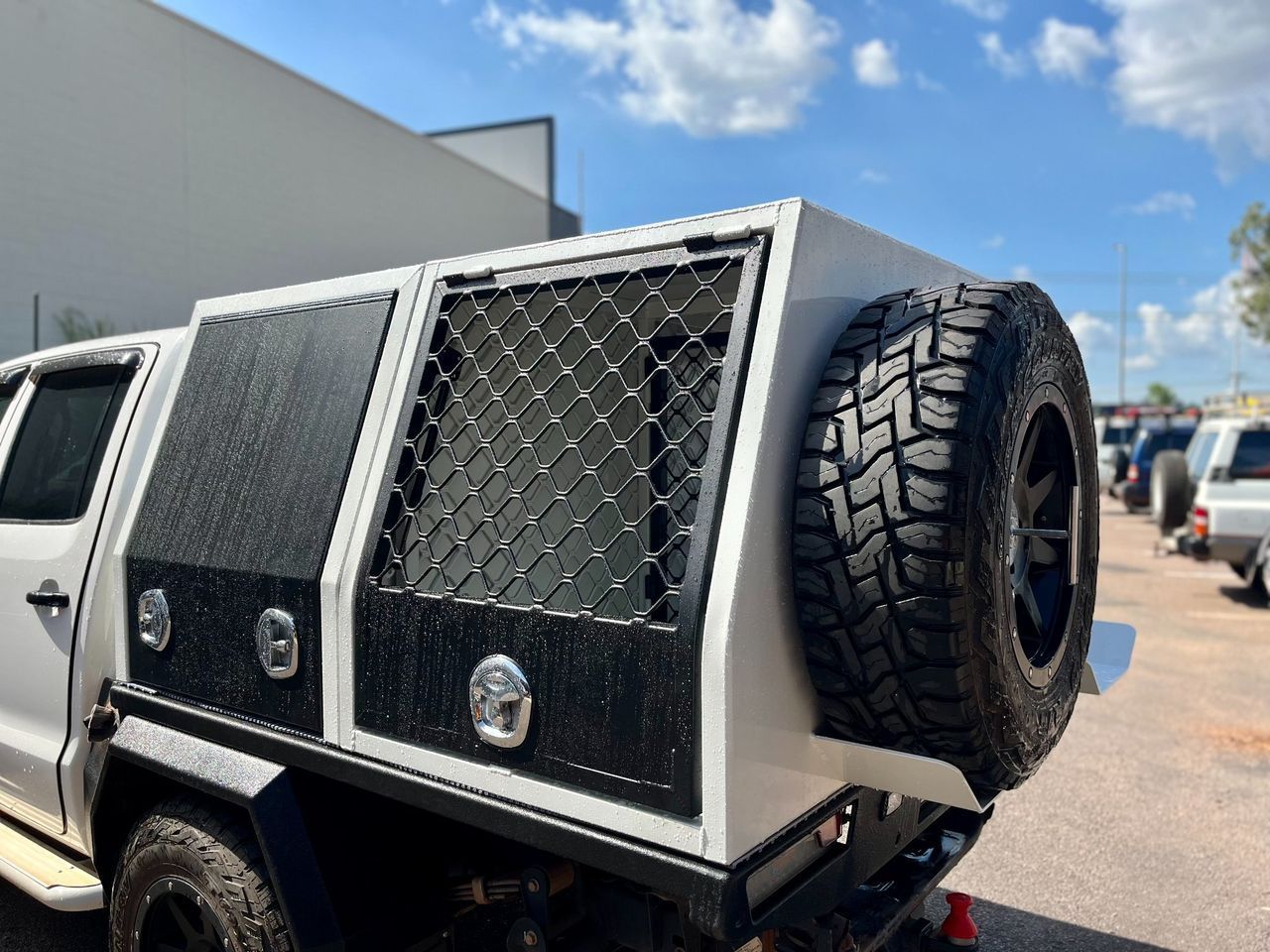 Custom pickup truck with armored side panels and a rear-mounted spare tire in a parking lot