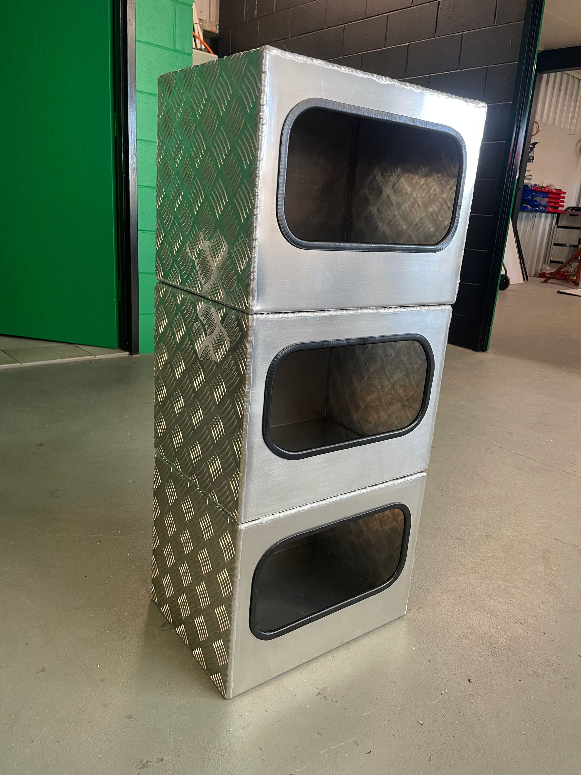 Three stacked silver metal boxes with oval openings, standing on a workshop floor.