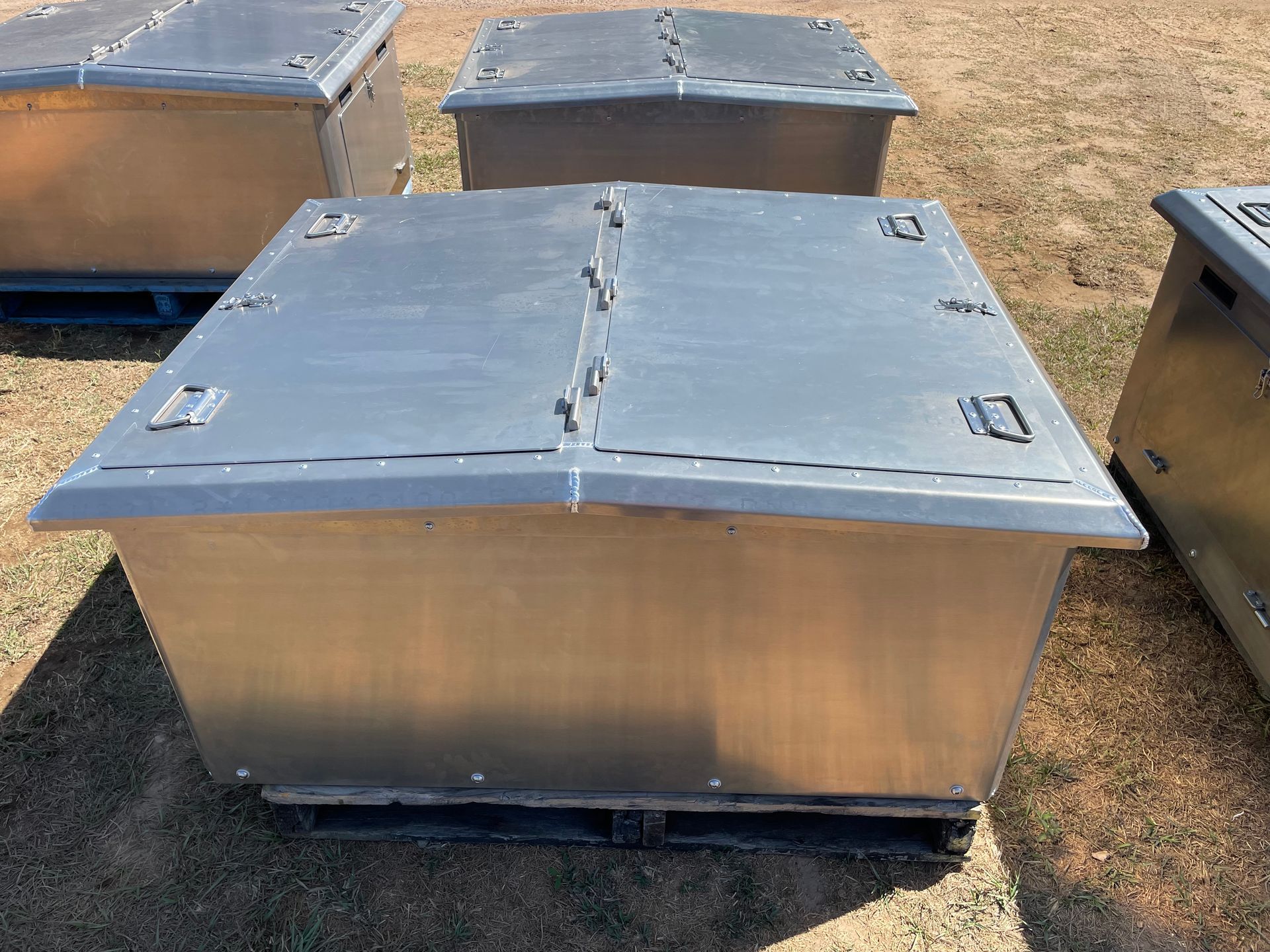 Metal storage boxes with gray lids arranged outdoors on dry grass.