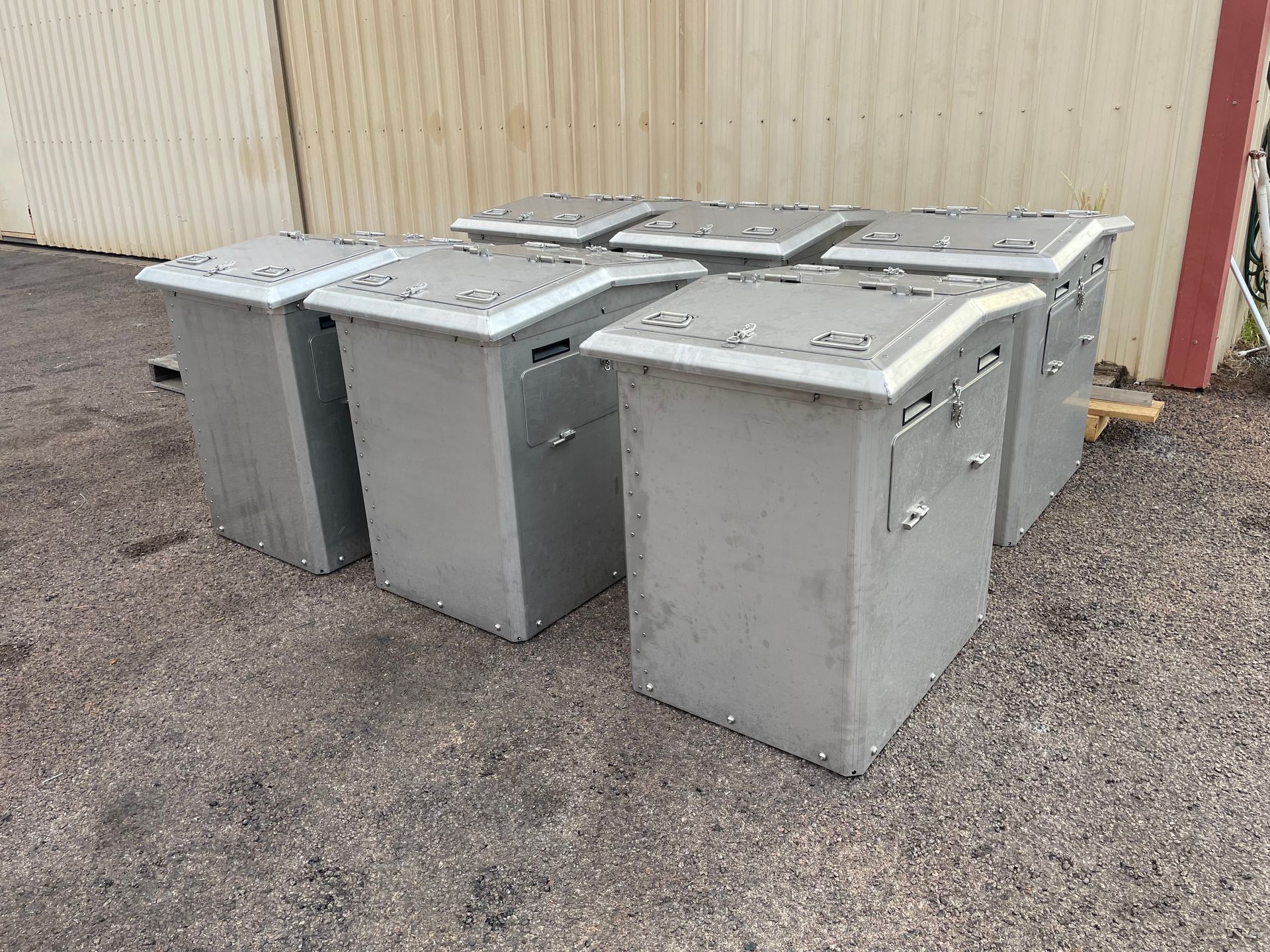 Three gray metal utility boxes on gravel beside a beige building.