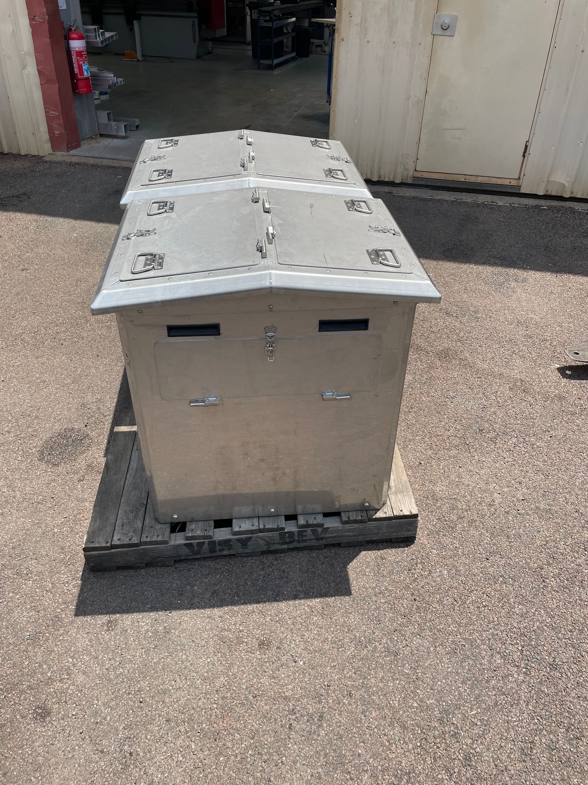 Metal shipping crate on a pallet in an outdoor industrial area with a curved, dented top cover.