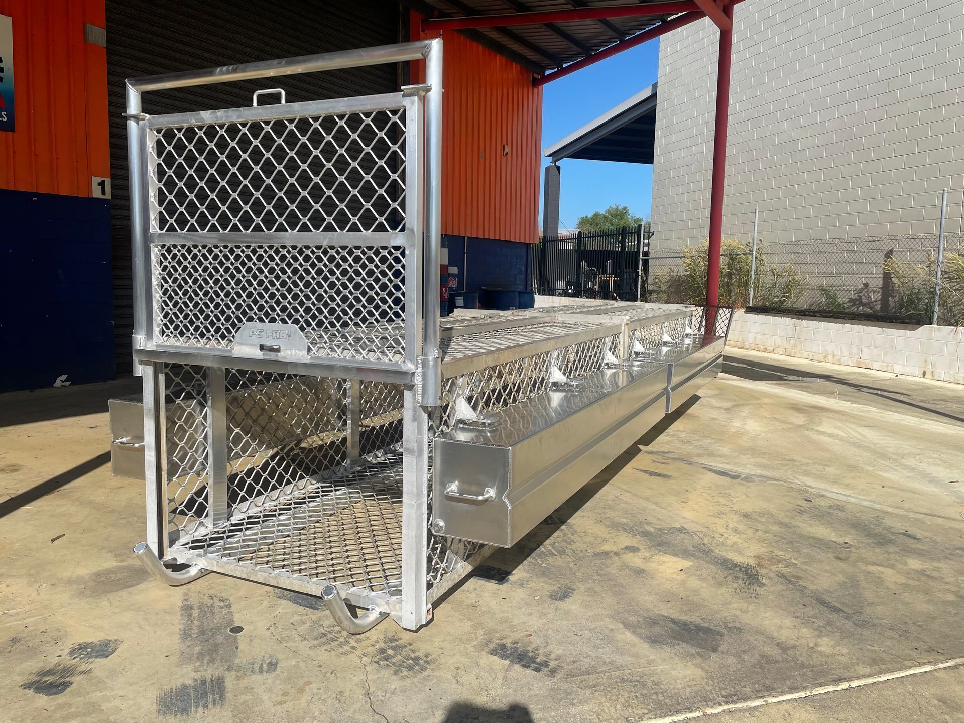 Metal chain-link livestock trailer ramp at a farm building, with aluminum side rails and mesh panels.