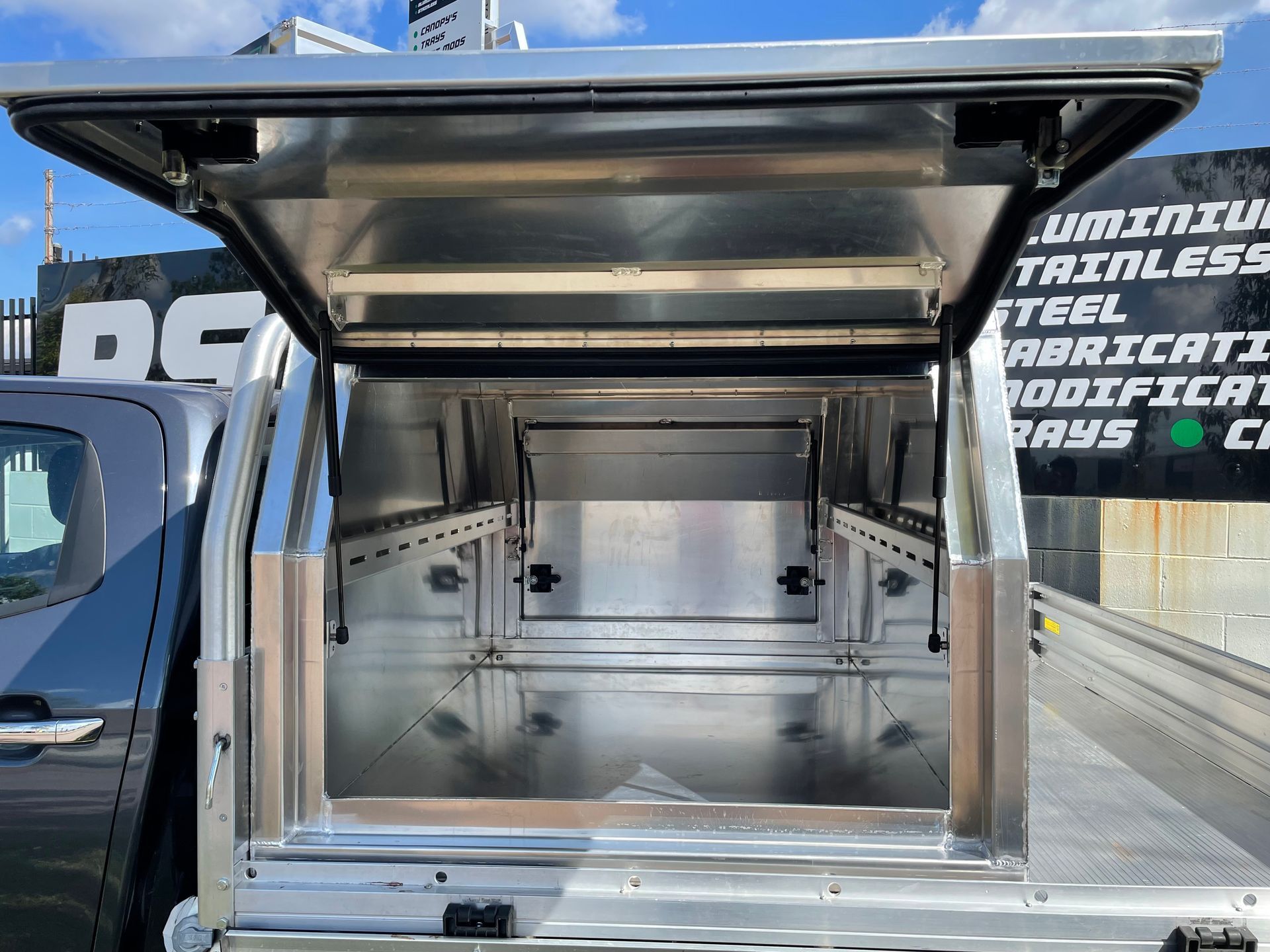 Open truck canopy with stainless steel interior, viewed from the rear on a vehicle lot