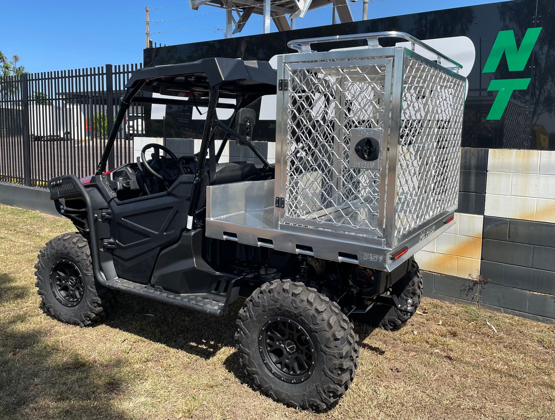 Black off-road utility vehicle with a silver cargo box parked on grass near a fence.