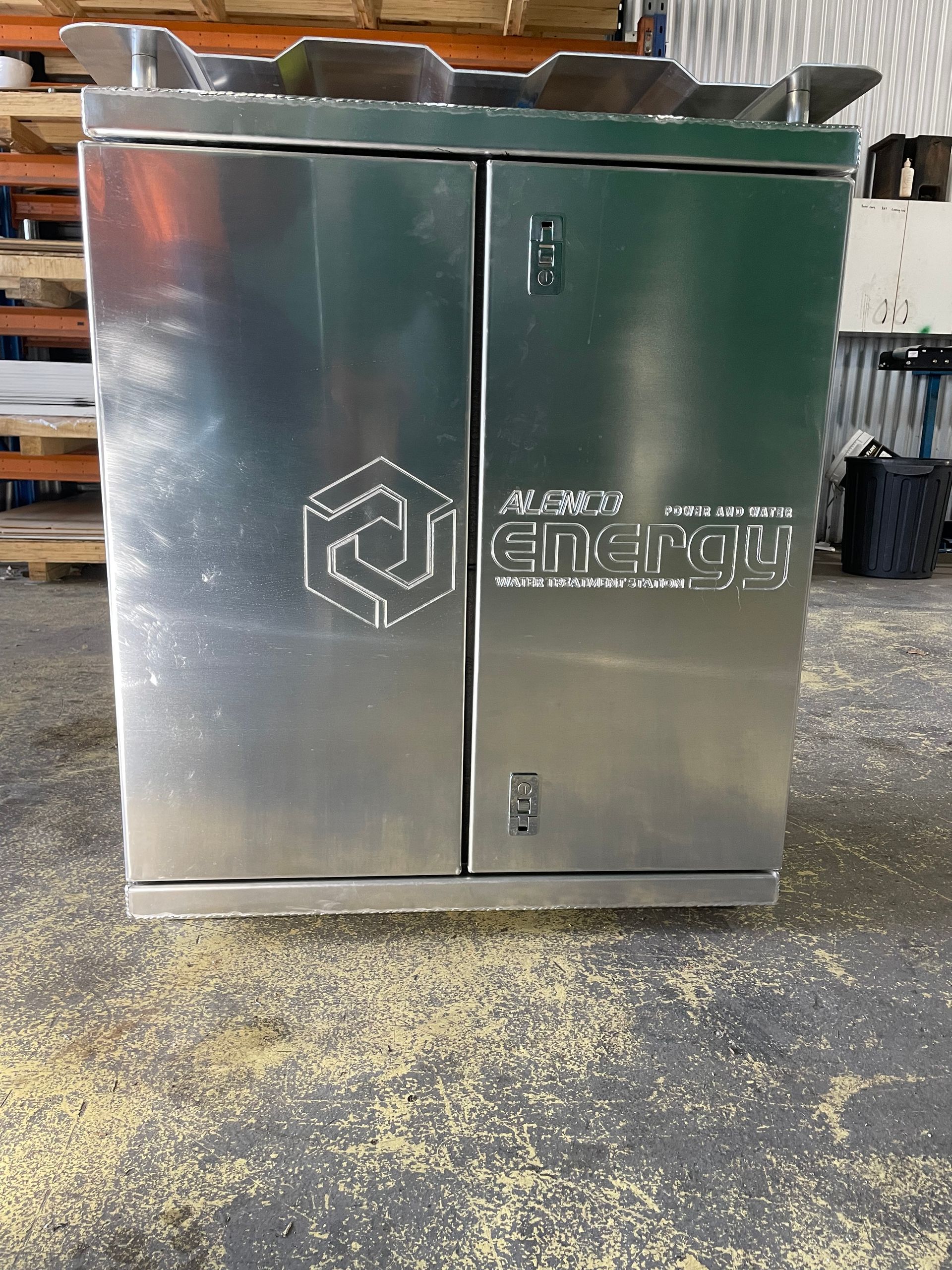 Stainless steel commercial cabinet with logo, sitting on a concrete floor in a workshop.
