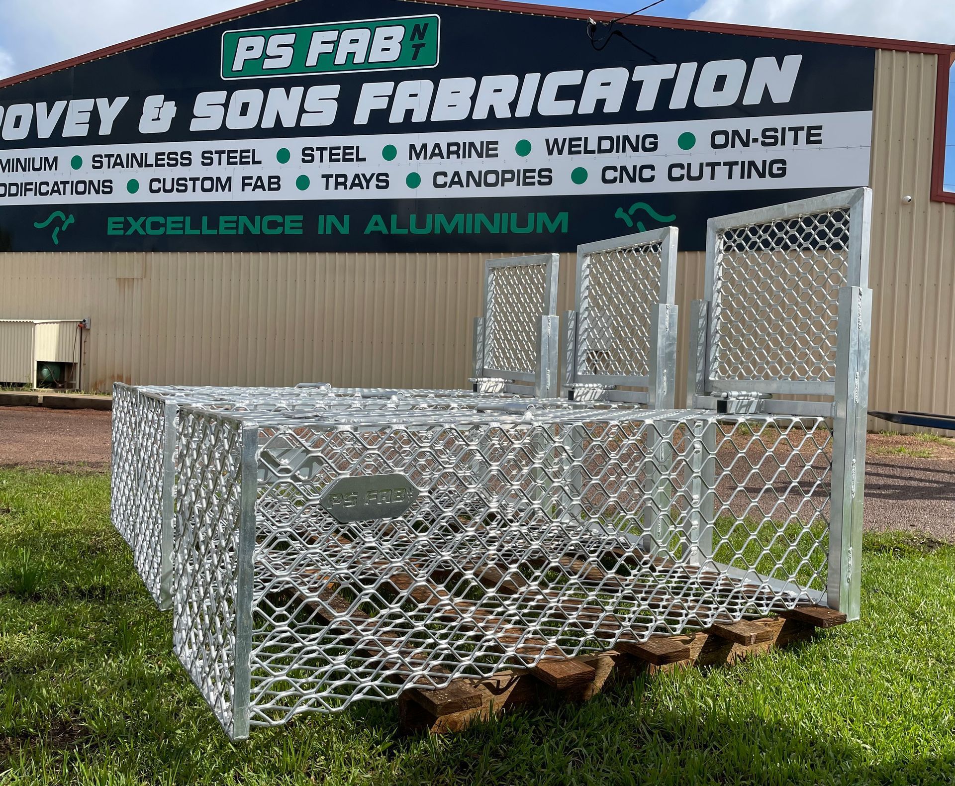 Shiny aluminum trailer frame on pallets in front of a fabrication shop sign