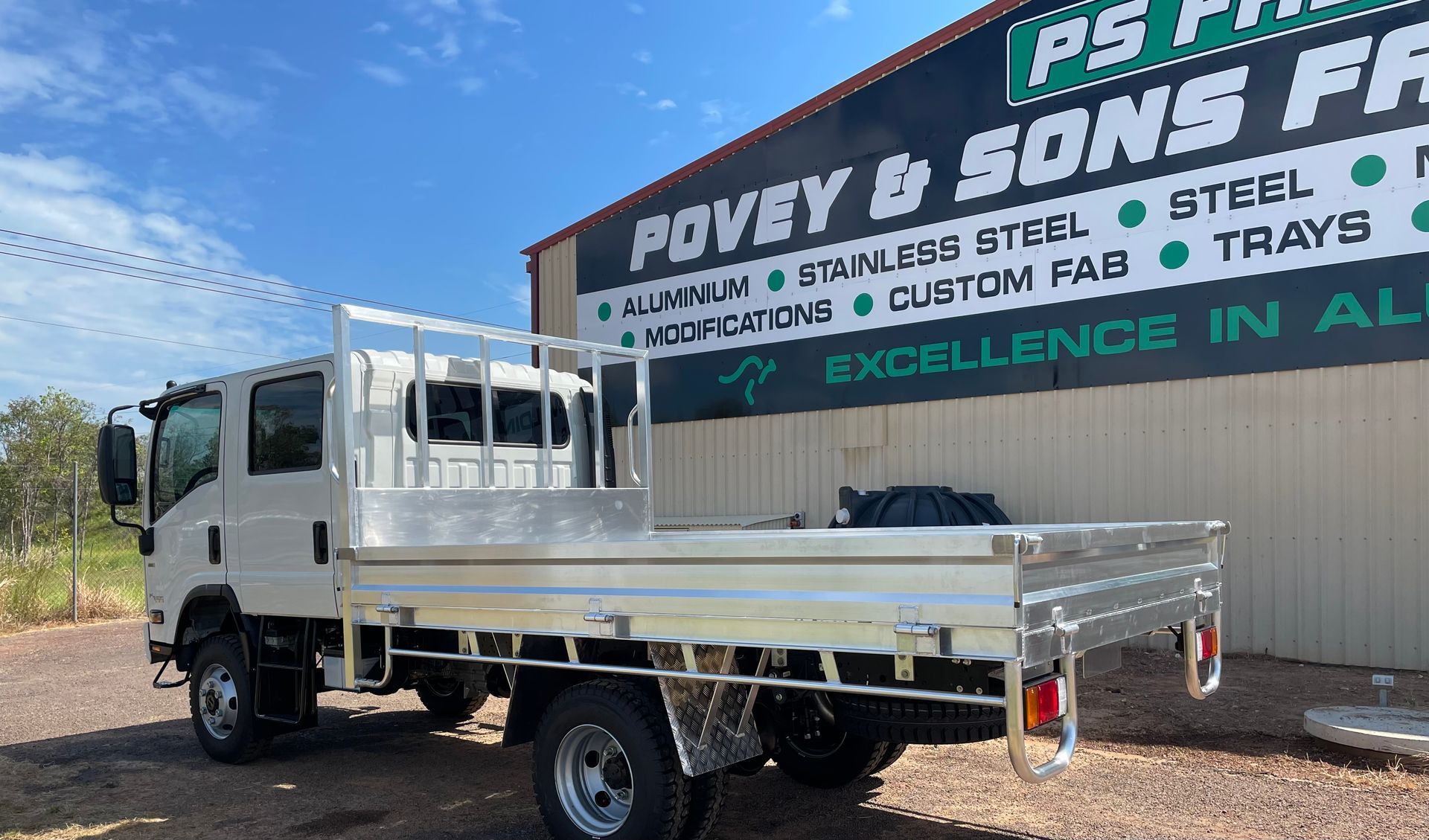 White flatbed truck parked beside a sign for Poyey & Sons Farm supplies under a blue sky
