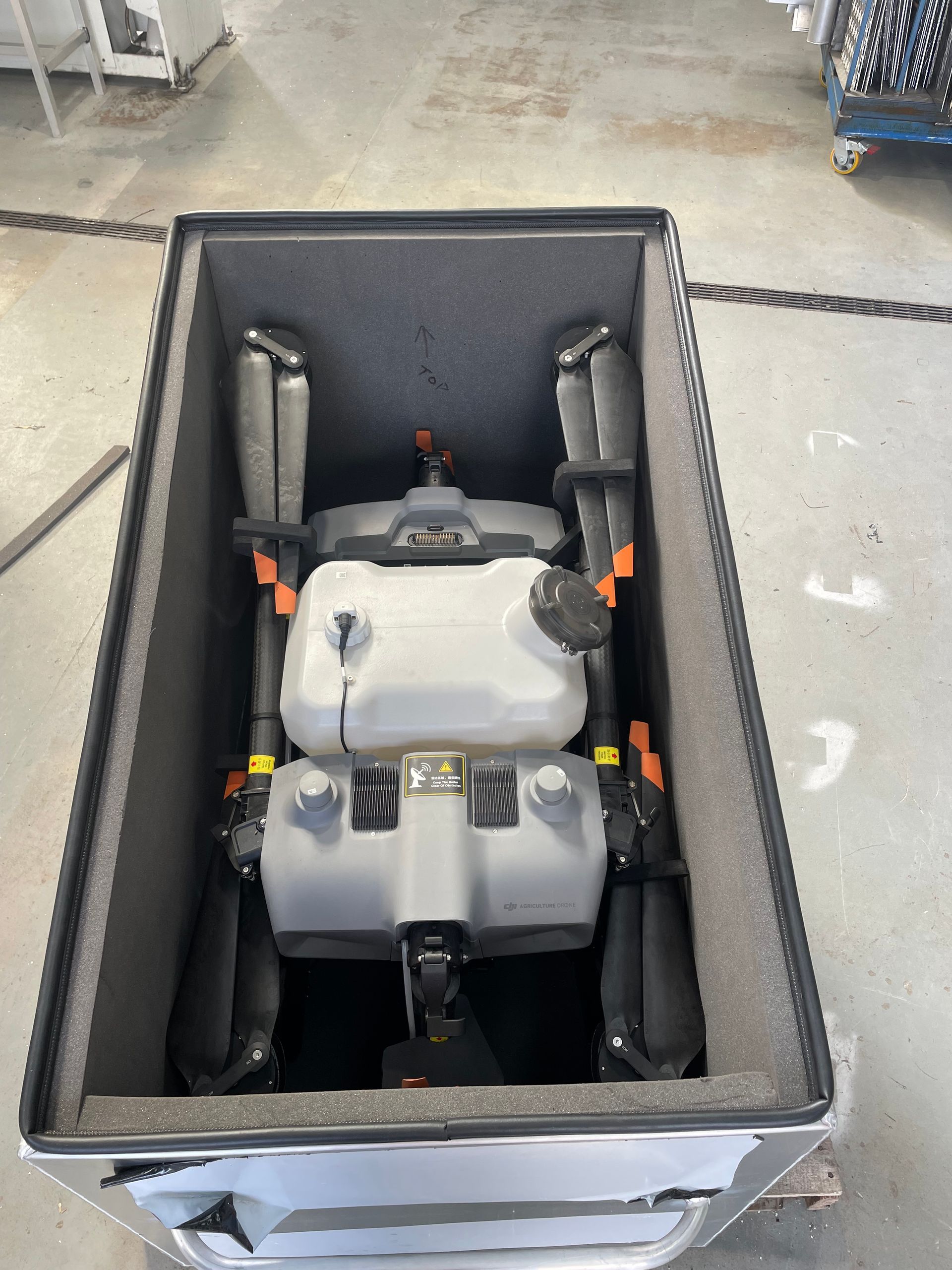 Gray machine secured in a black foam-lined shipping box on a workshop floor.