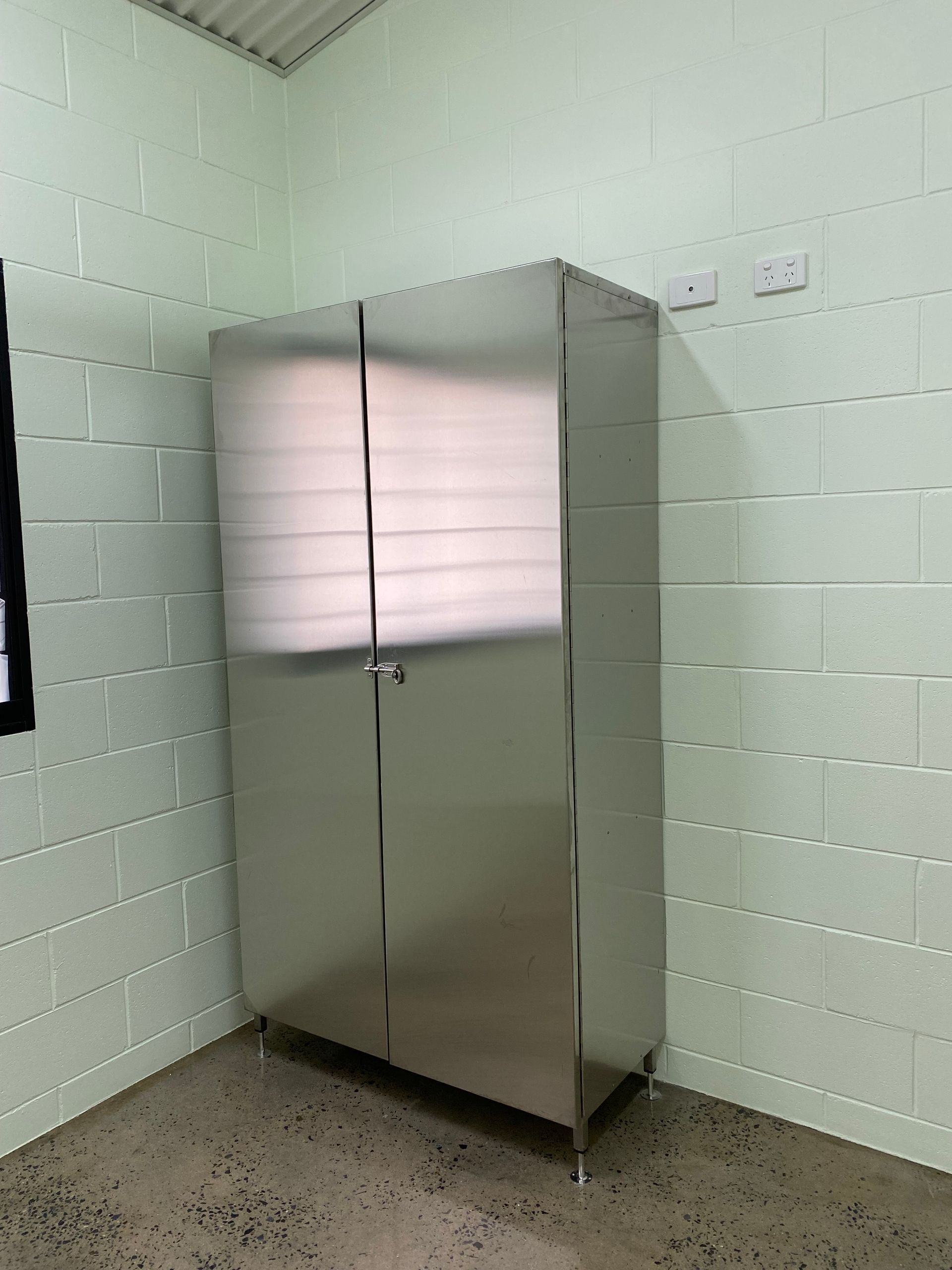 Stainless steel storage cabinet in a pale mint room with cinderblock walls and concrete floor.