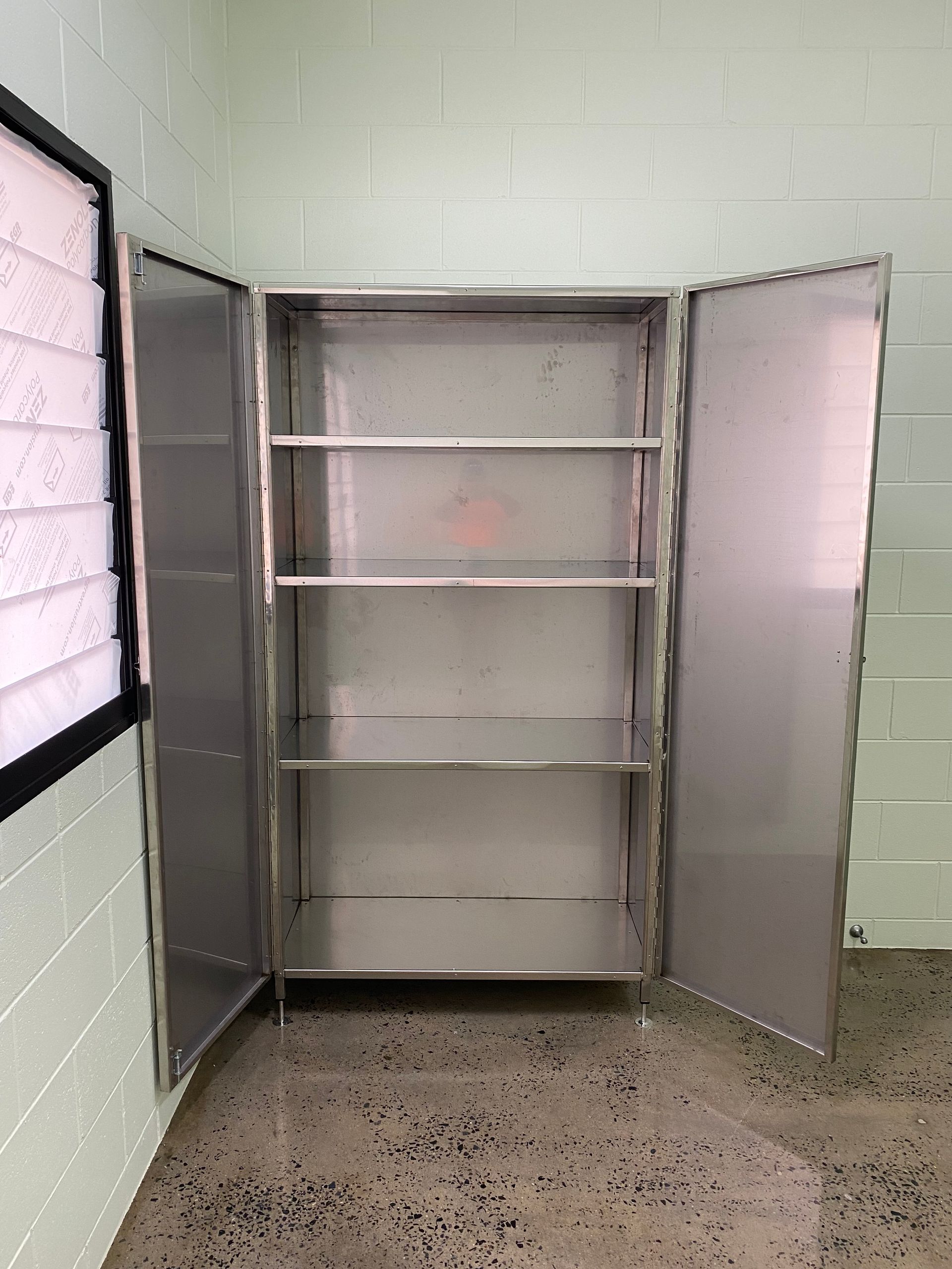 Open gray metal storage cabinet with shelves in a cinderblock room