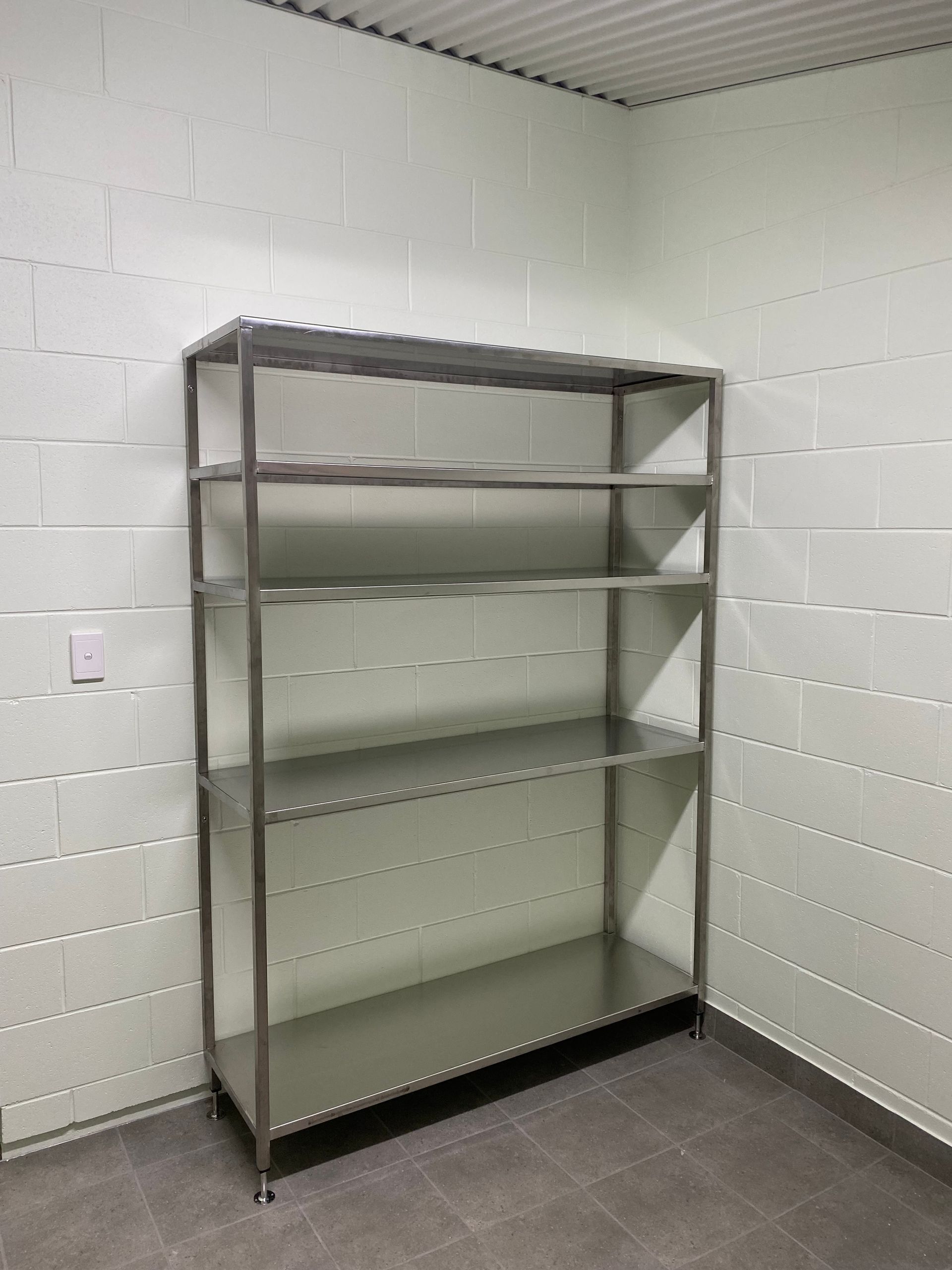 Empty metal shelving unit against a white cinderblock wall in a bare storage room.