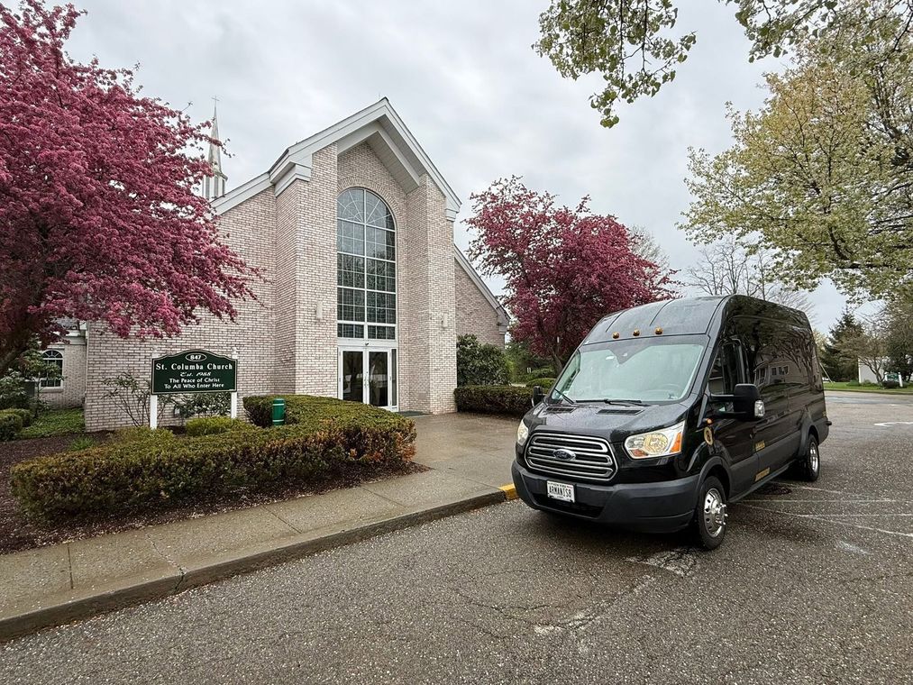 Black van parked outside a stone church with tall arched windows and pink flowering trees