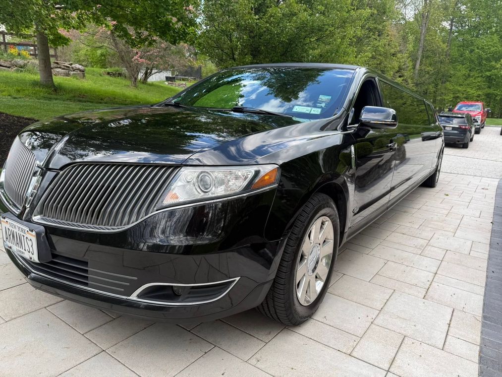 Black sedan parked on a tree-lined brick driveway with another car in the background
