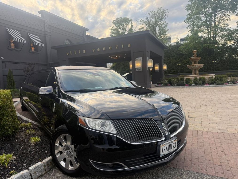 Black sedan parked outside a dark building with a driveway and fountain at dusk