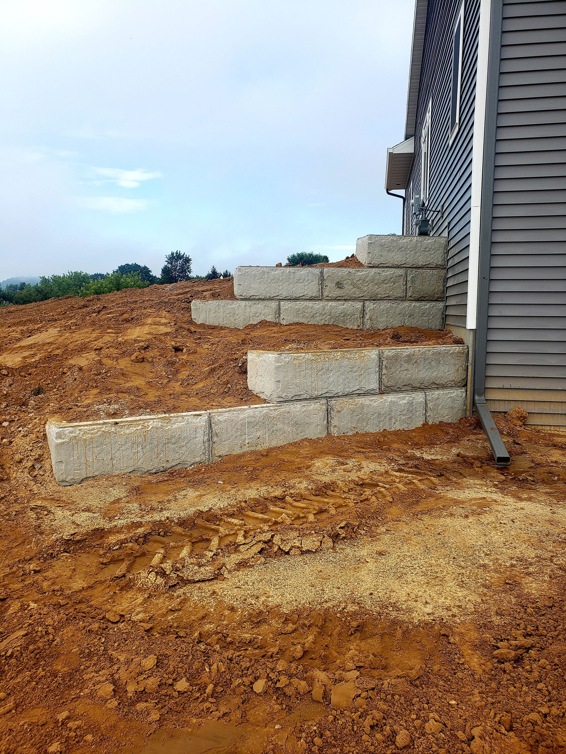 A house is sitting on top of a dirt hill next to a stone wall.